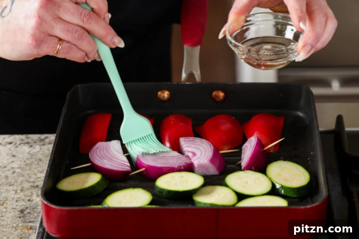 Zucchini, bell peppers, and onion wedges being placed onto a hot, oiled grill pan and brushed with more oil for grilling.