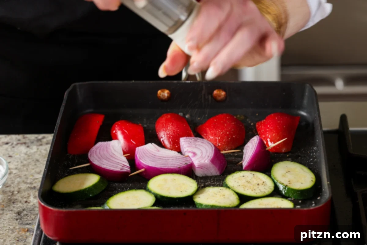 Freshly cracked black pepper being sprinkled over the vegetables on the grill pan, enhancing their flavor before cooking.