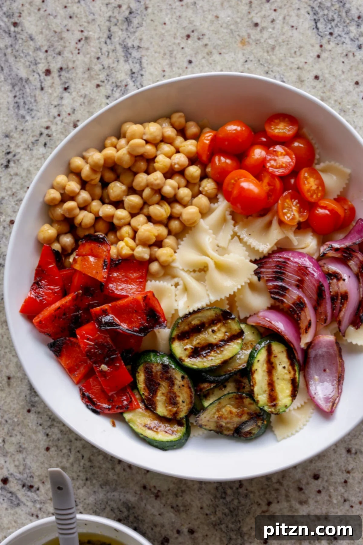 Close-up shot of a bowl of summer pasta salad, highlighting the vibrant colors and diverse ingredients like grilled zucchini, bell peppers, tomatoes, and pasta.