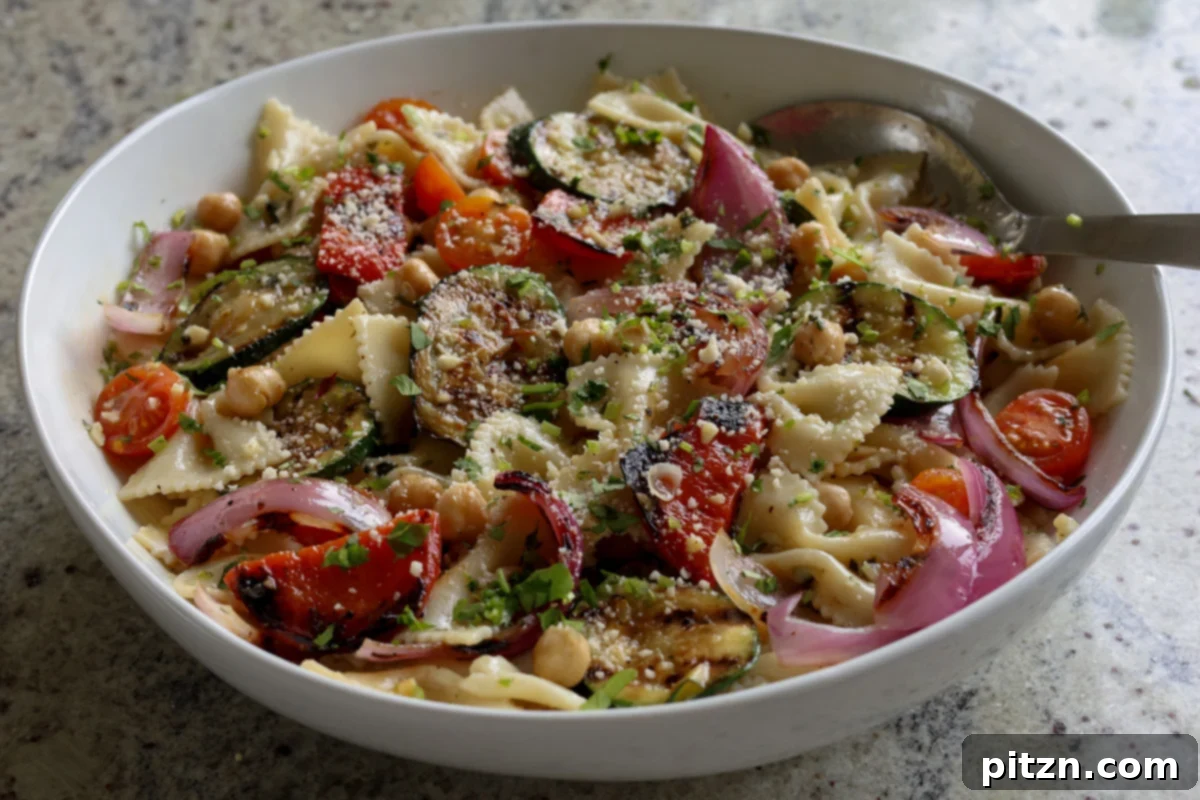 A close-up of the fully mixed pasta salad with grilled vegetables and chickpeas, garnished with vegan Parmesan, showcasing the vibrant colors and appealing textures.