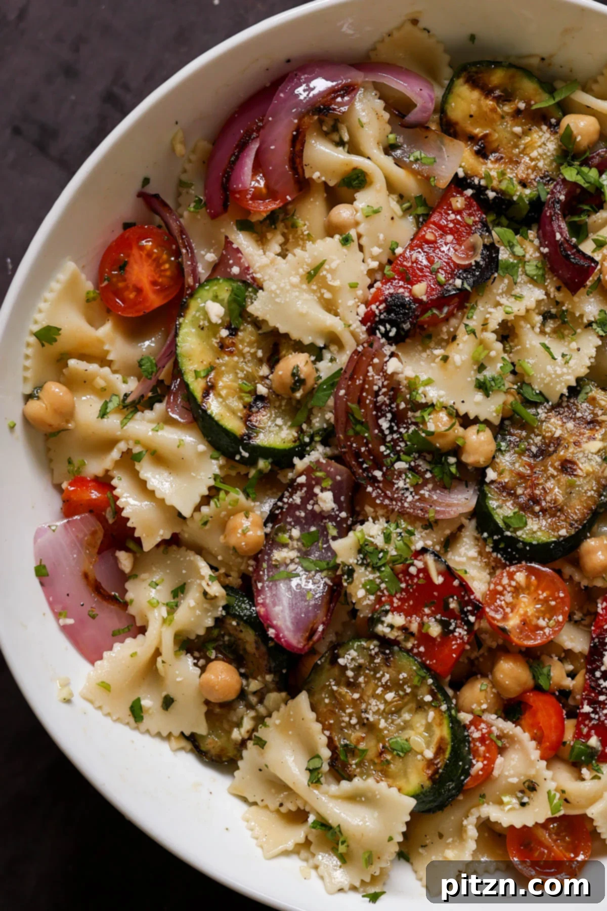 Close-up view of the summer pasta salad, highlighting the perfectly charred grilled vegetables and the vibrant green herbs.