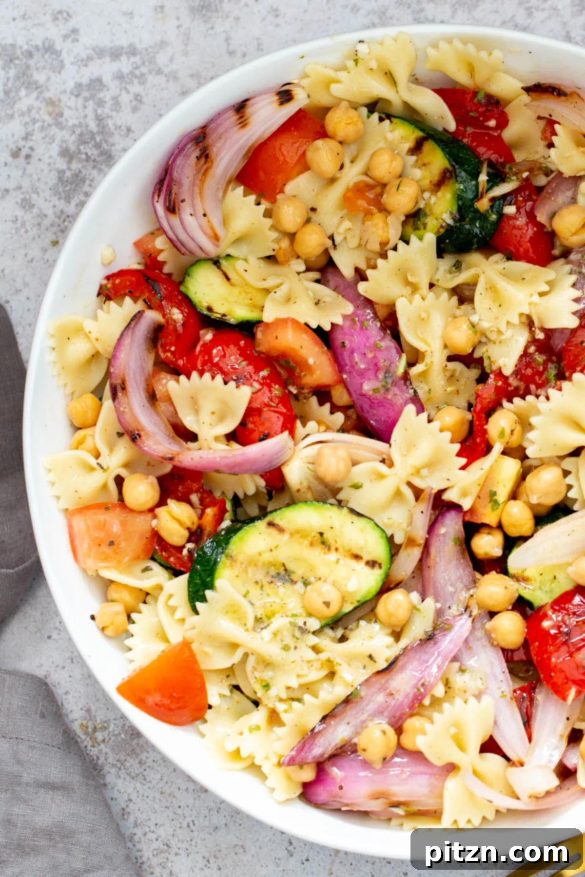 A large bowl of summer pasta salad, garnished with fresh basil and pepper flakes, ready to be served.