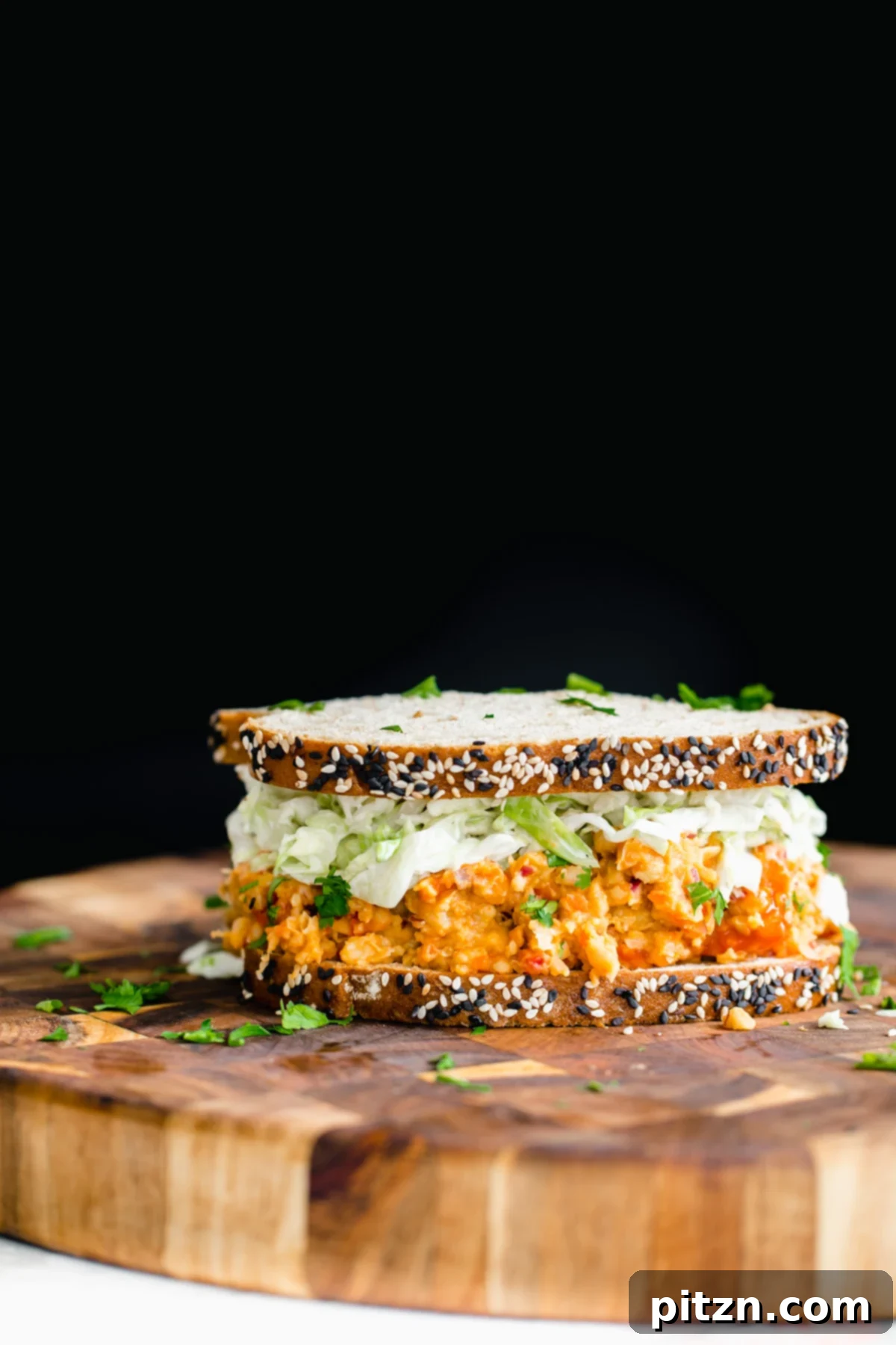An appetizing side view of a vegan Buffalo Chickpea Salad Sandwich on a rustic wooden board, ready to be enjoyed.