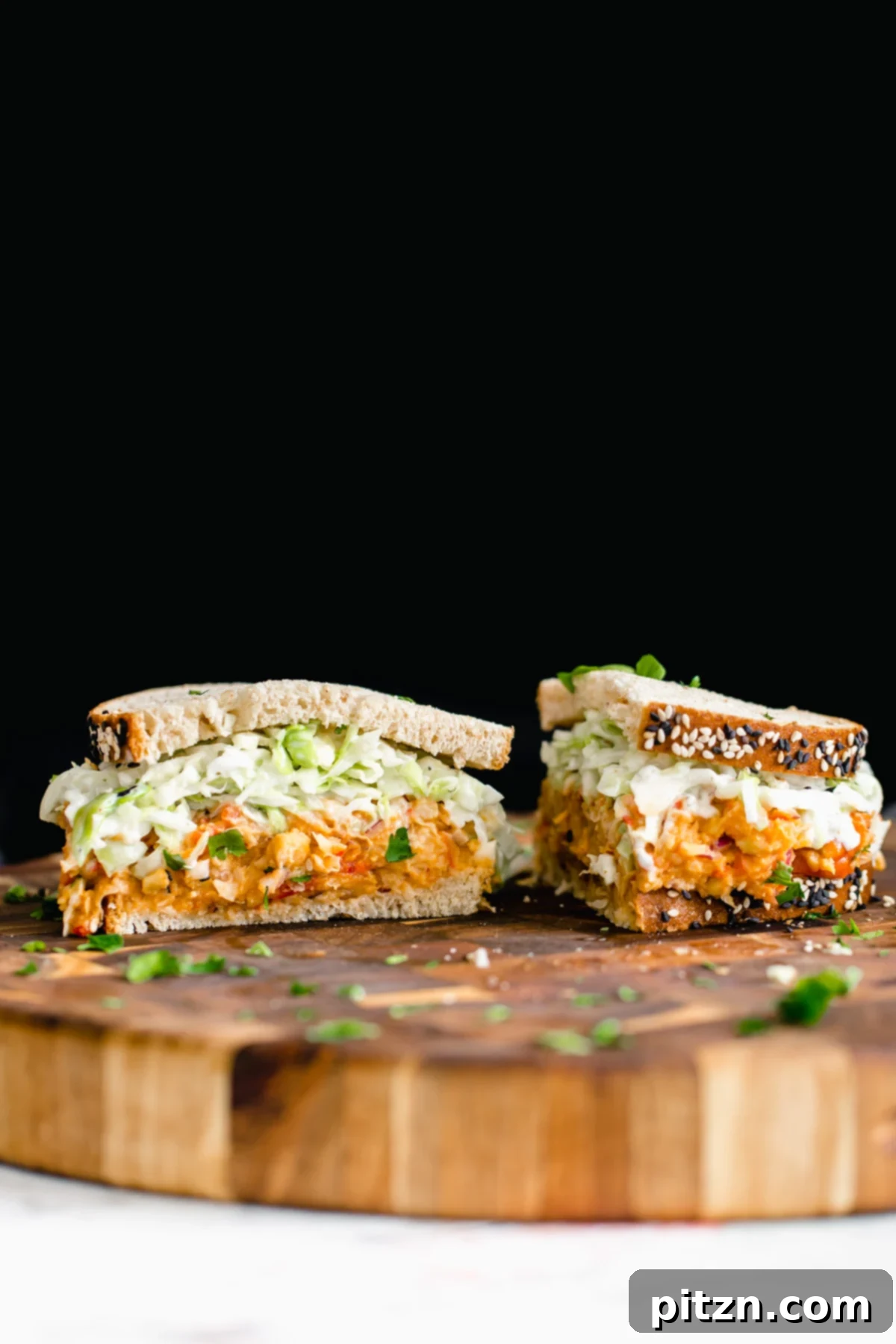 A close-up shot of a perfectly halved chickpea salad sandwich on a wooden board, ready for serving.