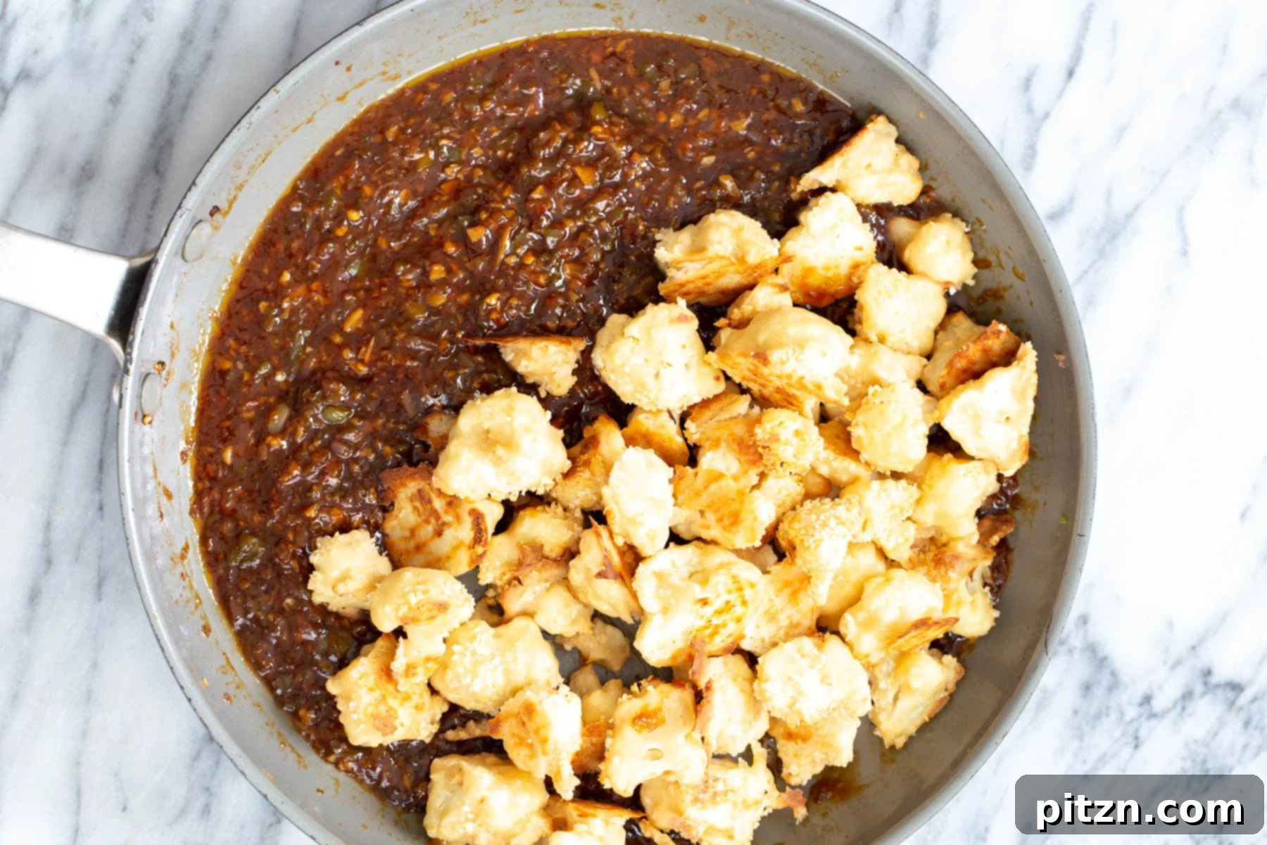 Golden Baked Cauliflower Manchurian 14 Crispy, breaded baked cauliflower florets being added to the rich Manchurian sauce in a pan, ready to be coated