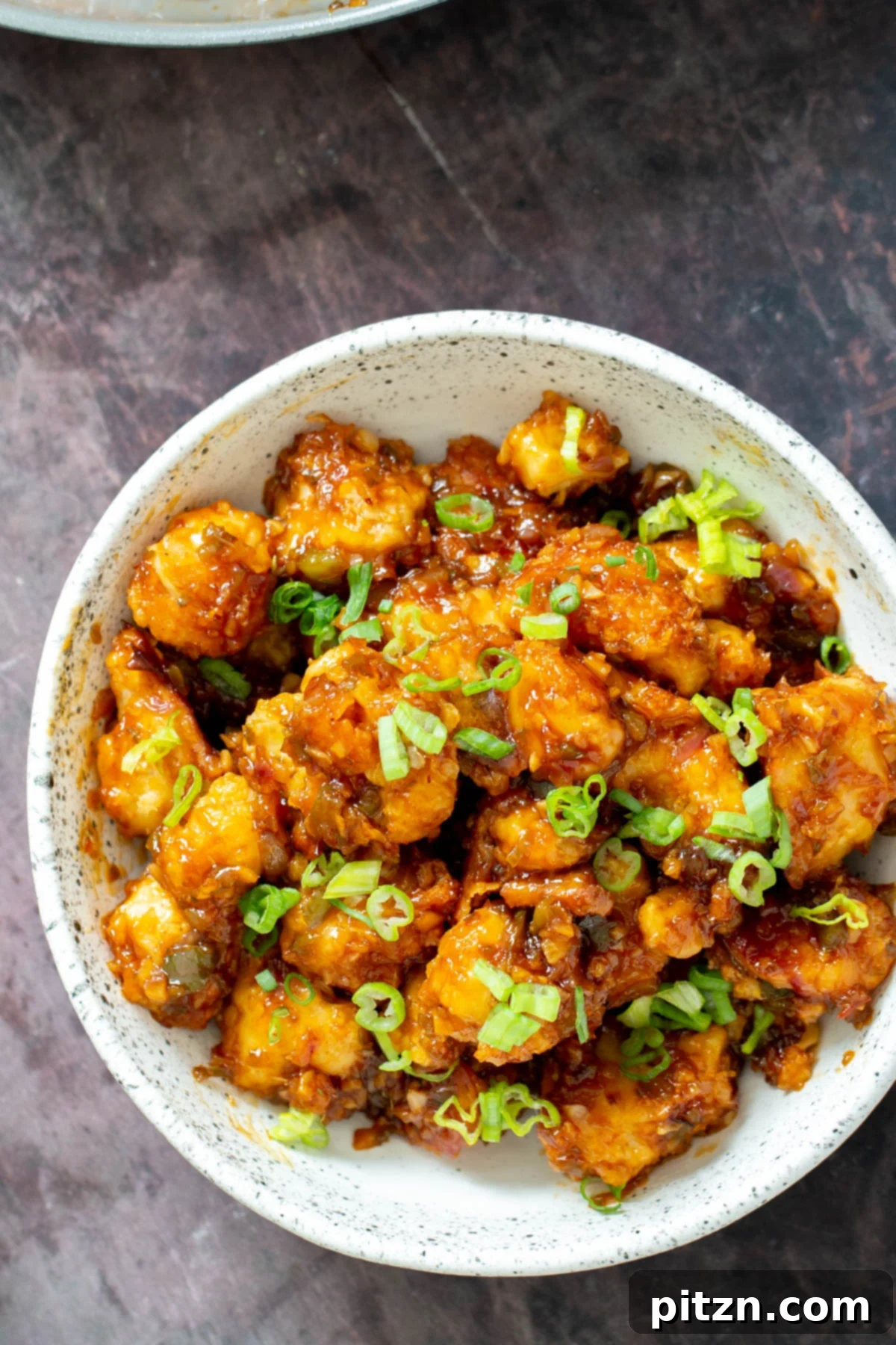 Golden Baked Cauliflower Manchurian 3 A white bowl brimming with vegan Gobi Manchurian, generously topped with thinly sliced scallions for freshness