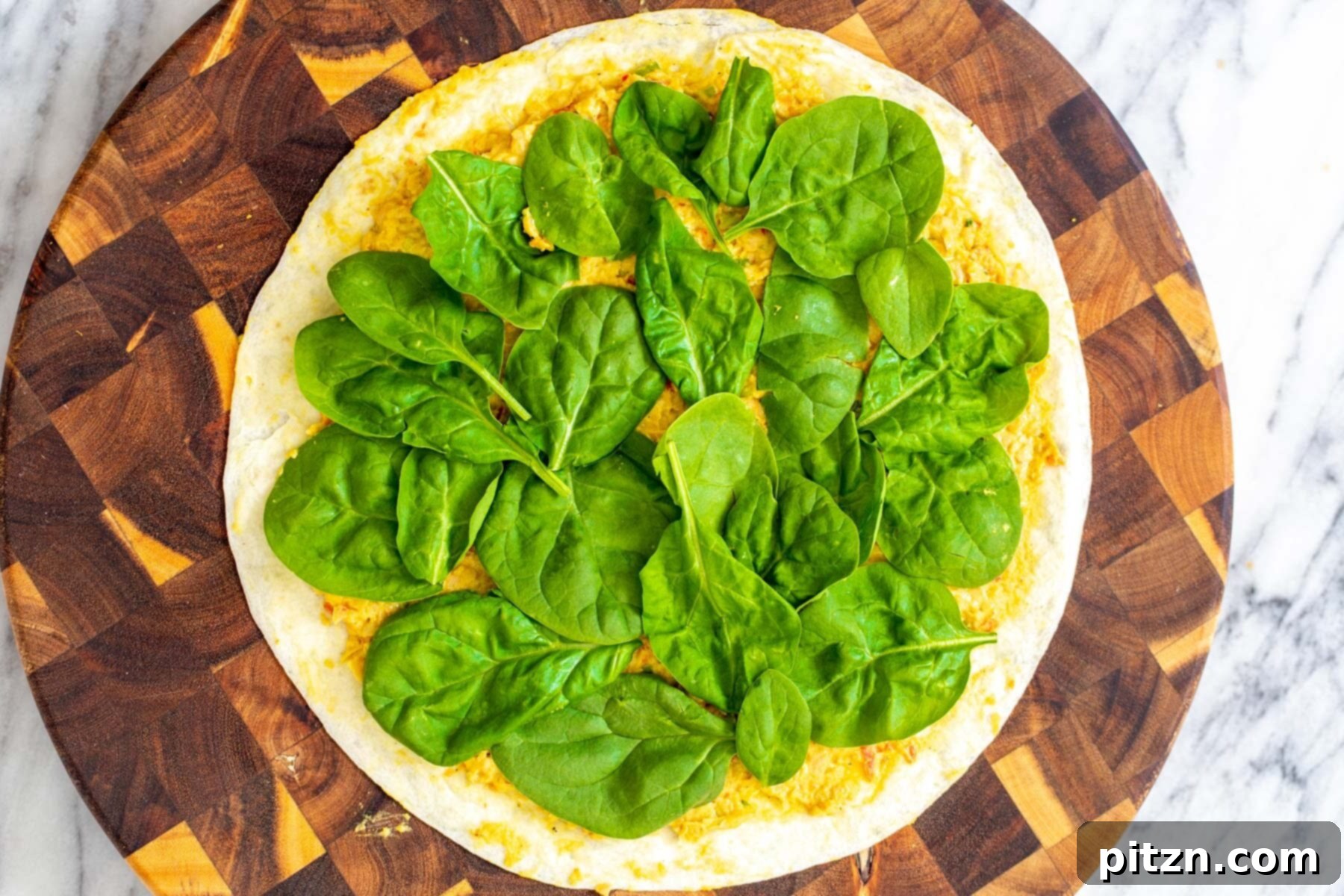 chickpea breakfast tortilla topped with chickpea scramble and fresh spinach on a wooden board