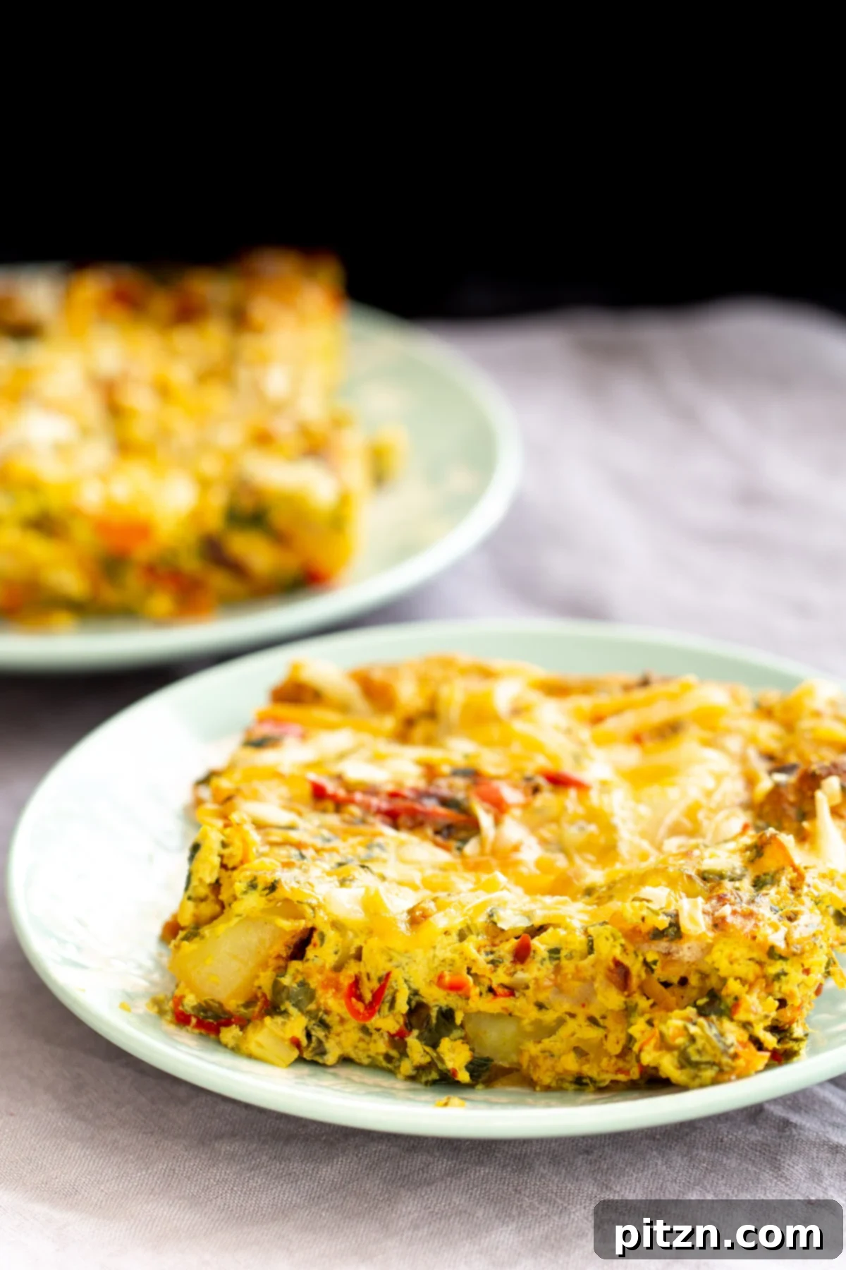 Two plates with generous servings of Vegan Mexican Egg Casserole, showcasing roasted vegetables, fluffy tofu eggs, and melted vegan cheese.