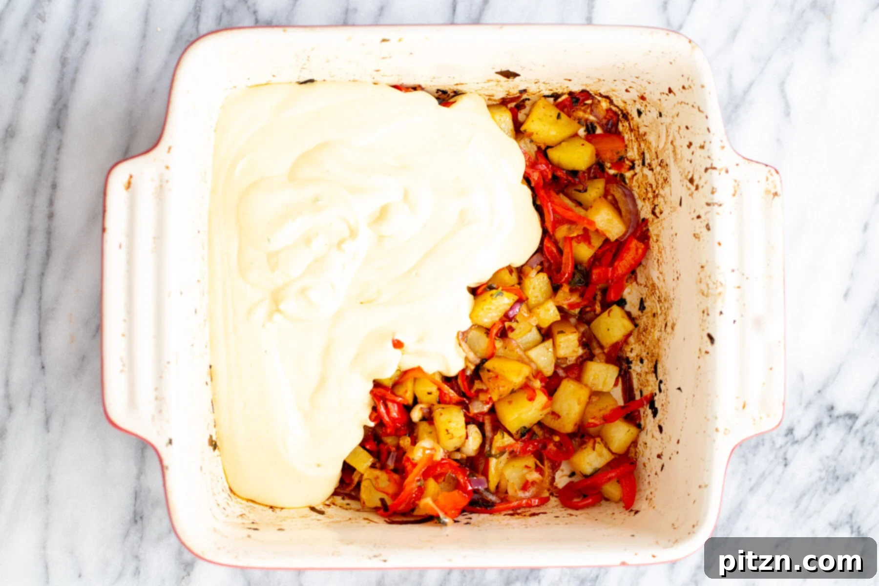 The smooth vegan egg mixture is being carefully poured over the roasted vegetables in the casserole dish, preparing for the final bake.
