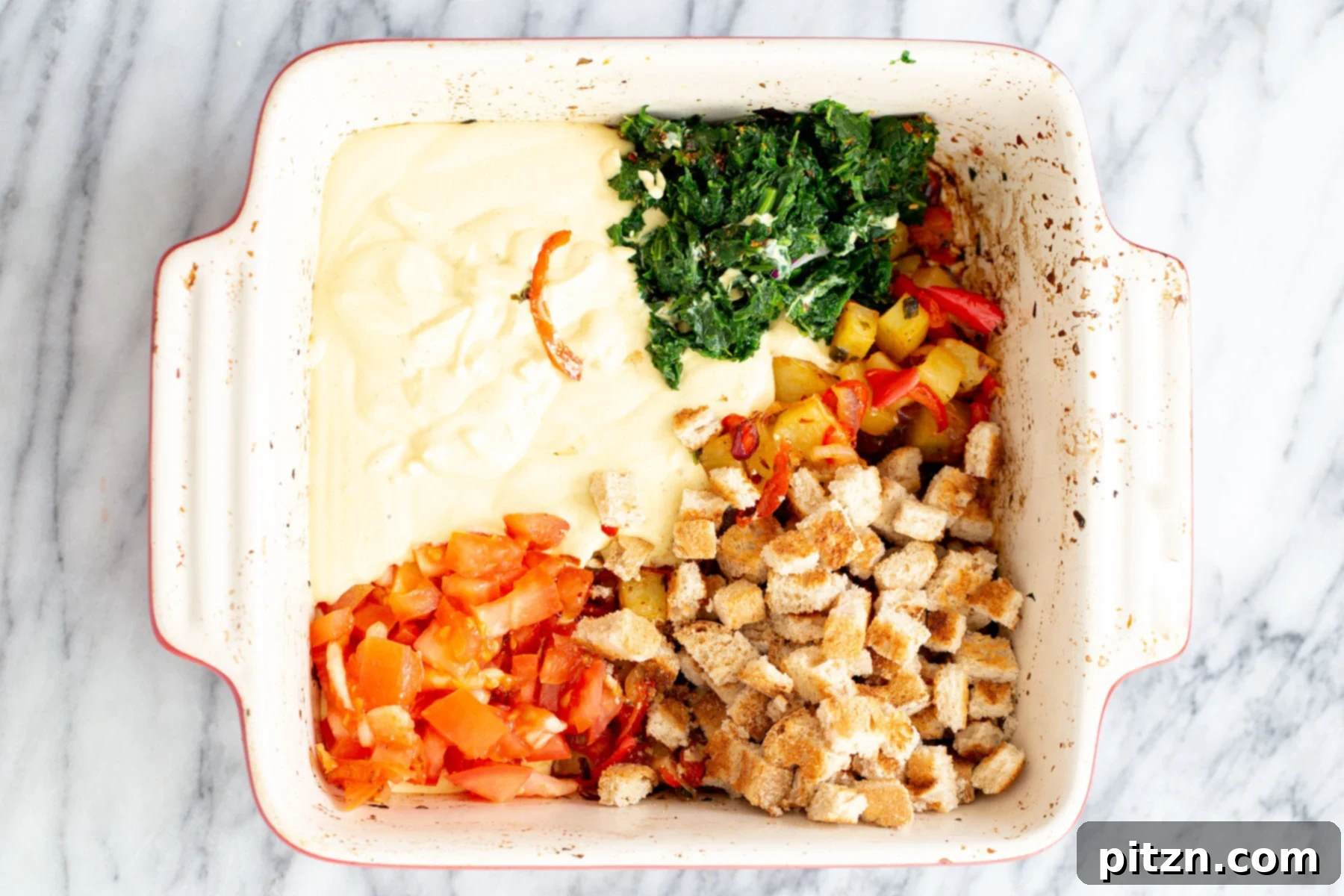 Bread cubes, fresh spinach, and chopped tomatoes are added to the vegan egg and vegetable mixture in the casserole dish.