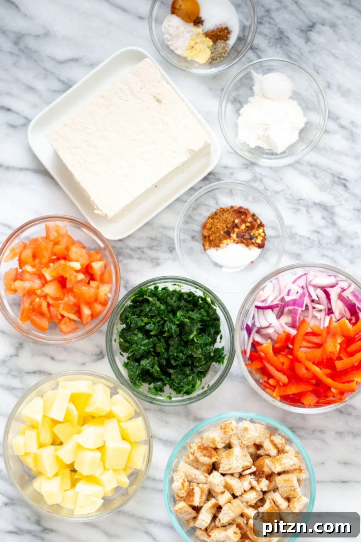 A variety of fresh ingredients laid out for making vegan Mexican egg casserole, including potatoes, onions, bell peppers, spinach, and tofu.