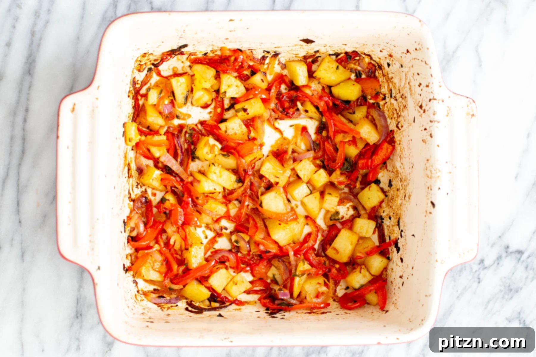 Roasted bell peppers, onion, and potatoes, slightly browned and tender, in a casserole dish after their initial bake.