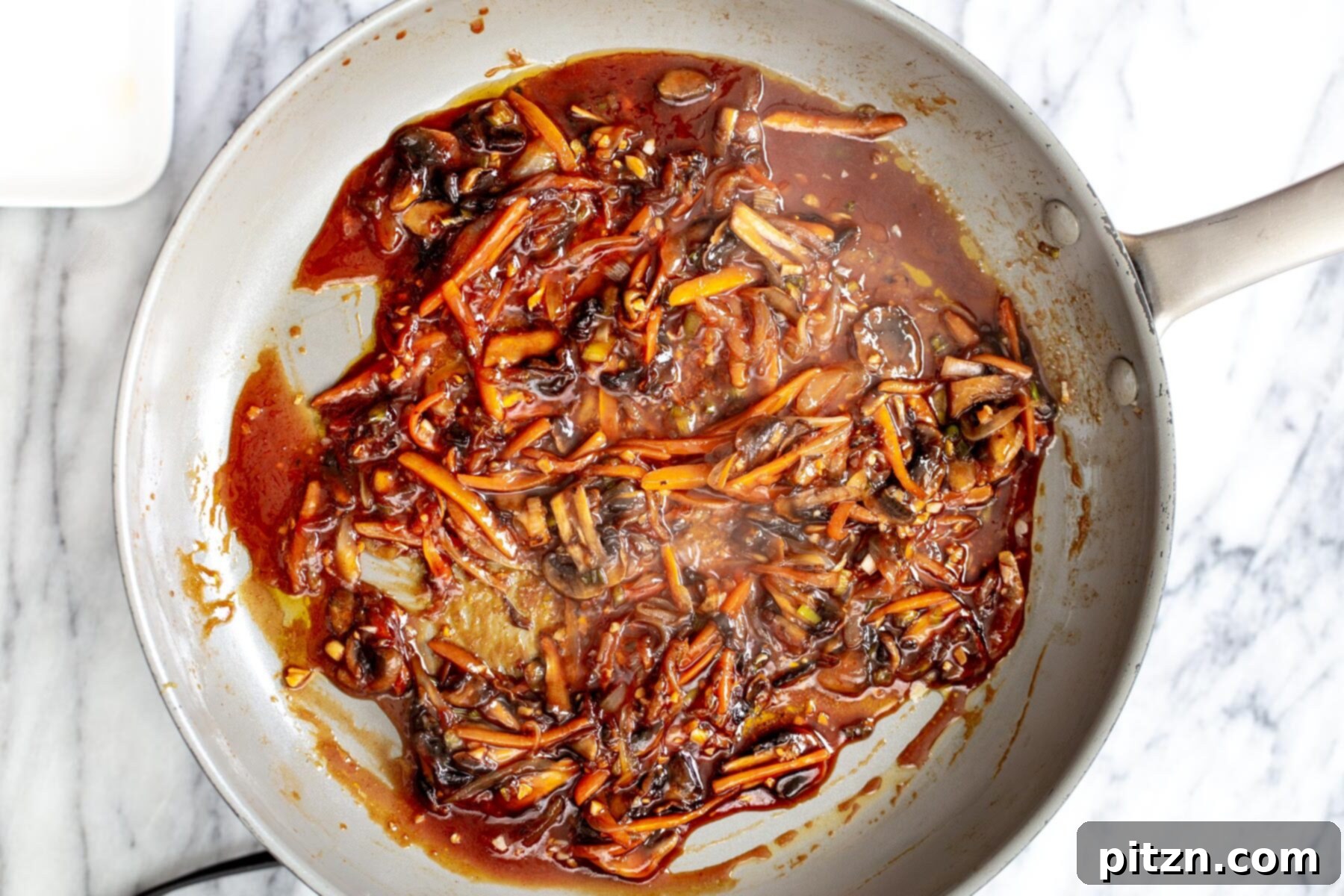 Veggies simmering vigorously in the rich, red gochujang sauce within a saucepan, illustrating the flavor development of the Korean stir-fry.