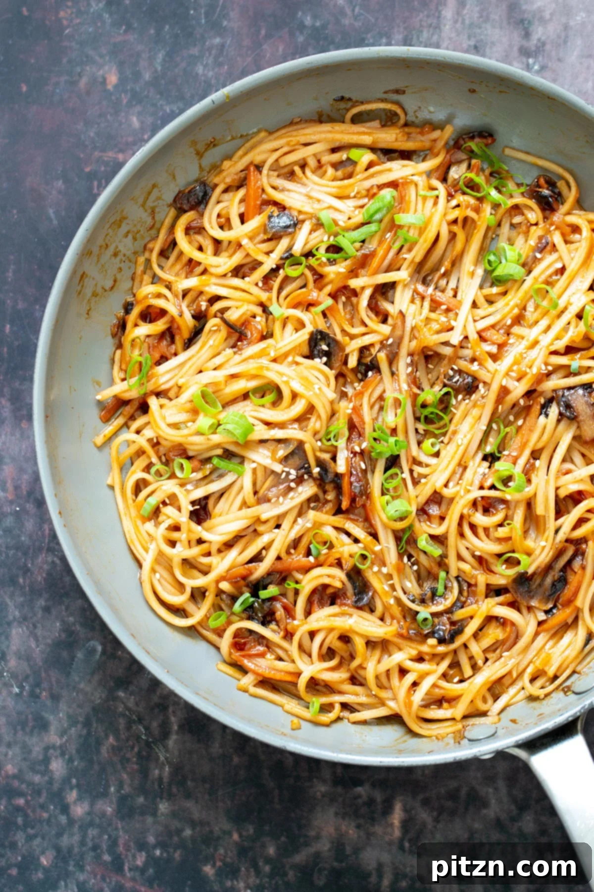 A close-up view of Gochujang Noodles and mushrooms simmering in a pan, adorned with thinly sliced spring onions, illustrating the delightful cooking process.