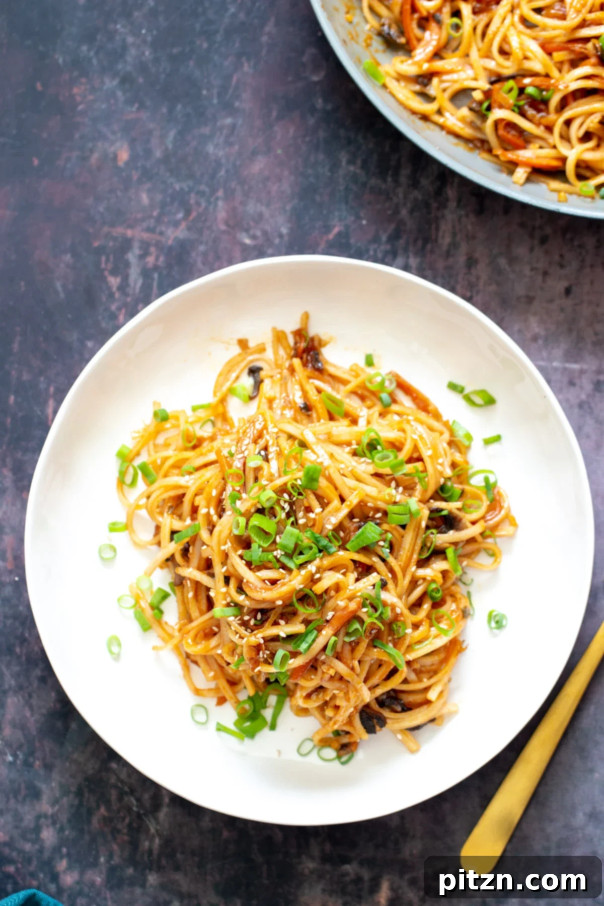 A tempting plate of gochujang noodles, generously topped with freshly sliced spring onions and a sprinkle of sesame seeds, highlighting its vibrant presentation.