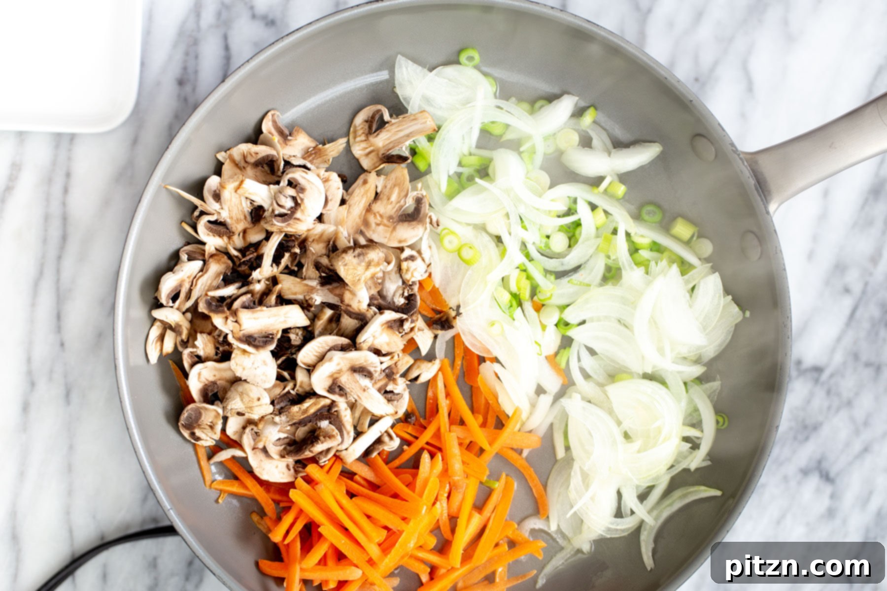 A visual of sliced onions, julienne carrots, mushrooms, and the white parts of spring onions sautéing in a hot saucepan, forming the base of the stir-fry.