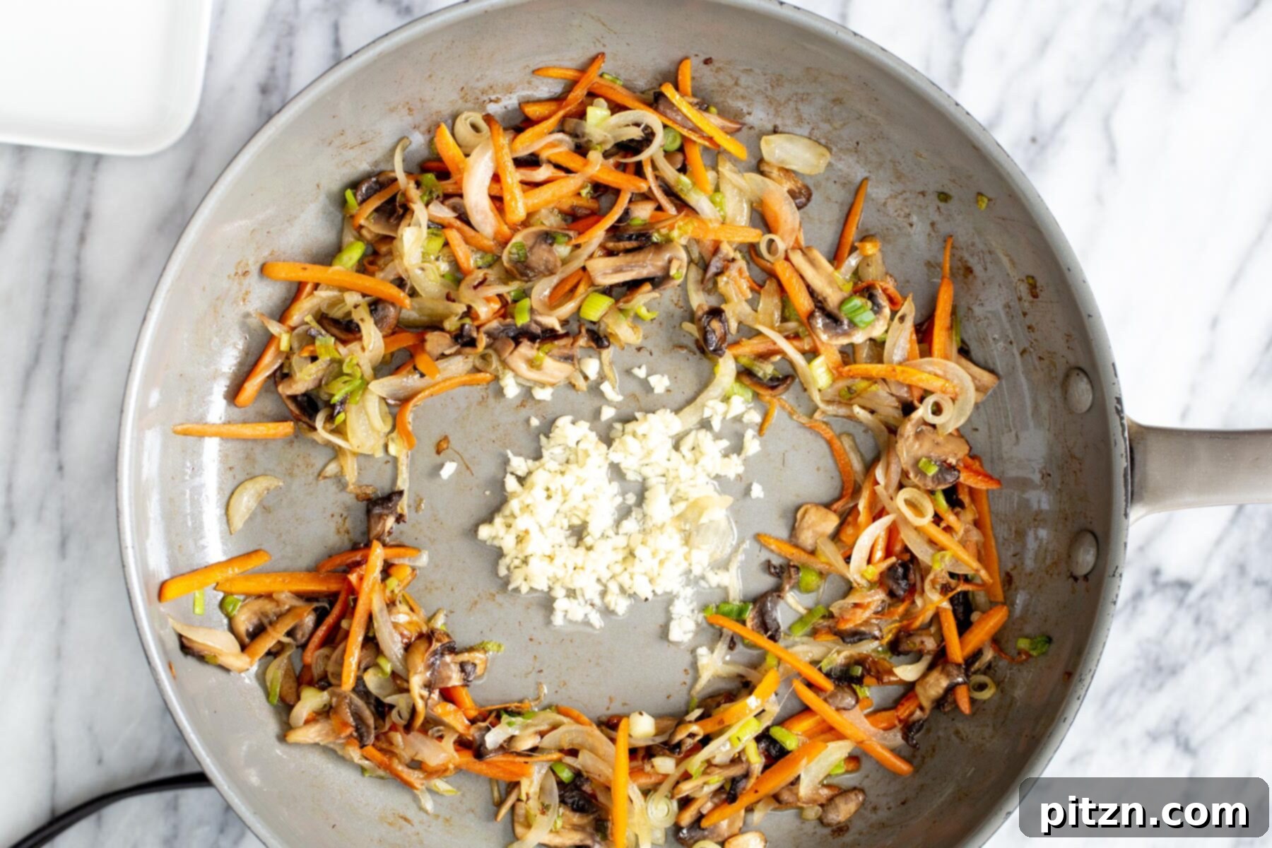 The process of stir-frying finely sliced vegetables with fragrant minced garlic in a saucepan, creating an aromatic foundation for the noodle dish.