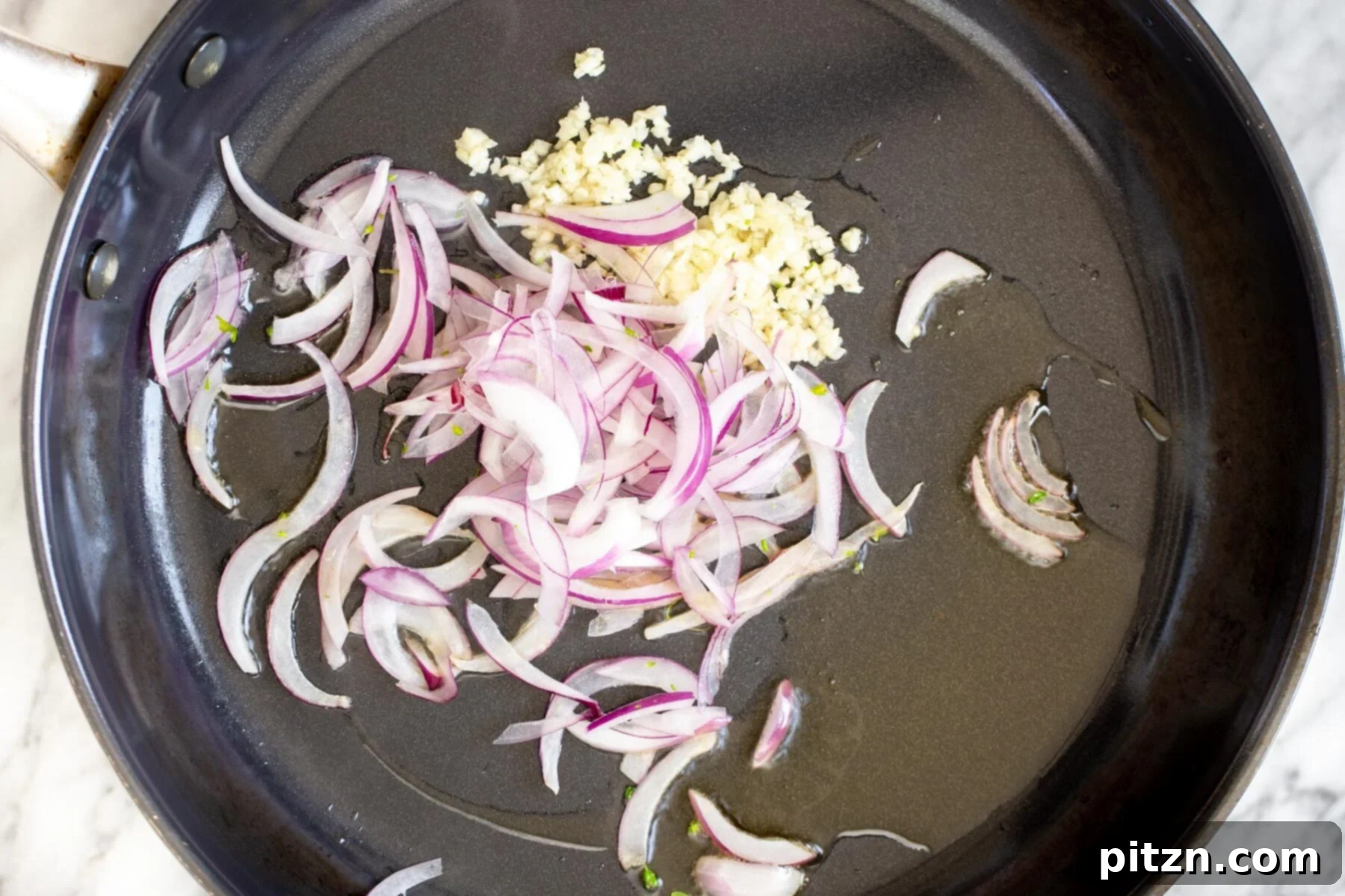 Minced garlic and thinly sliced shallots sautéing in a hot frying pan with sesame oil