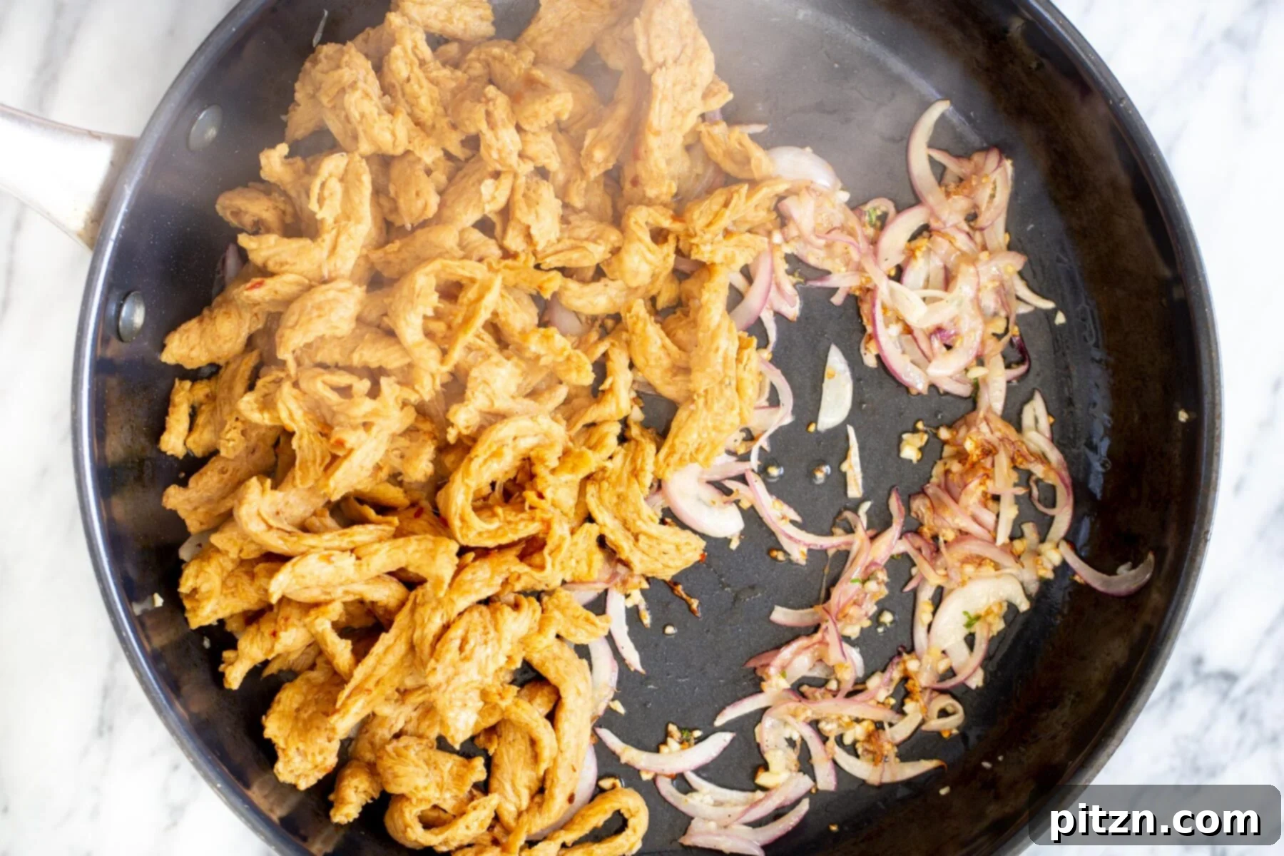 Rehydrated soy curls added to a frying pan with golden garlic and onions, ready for searing