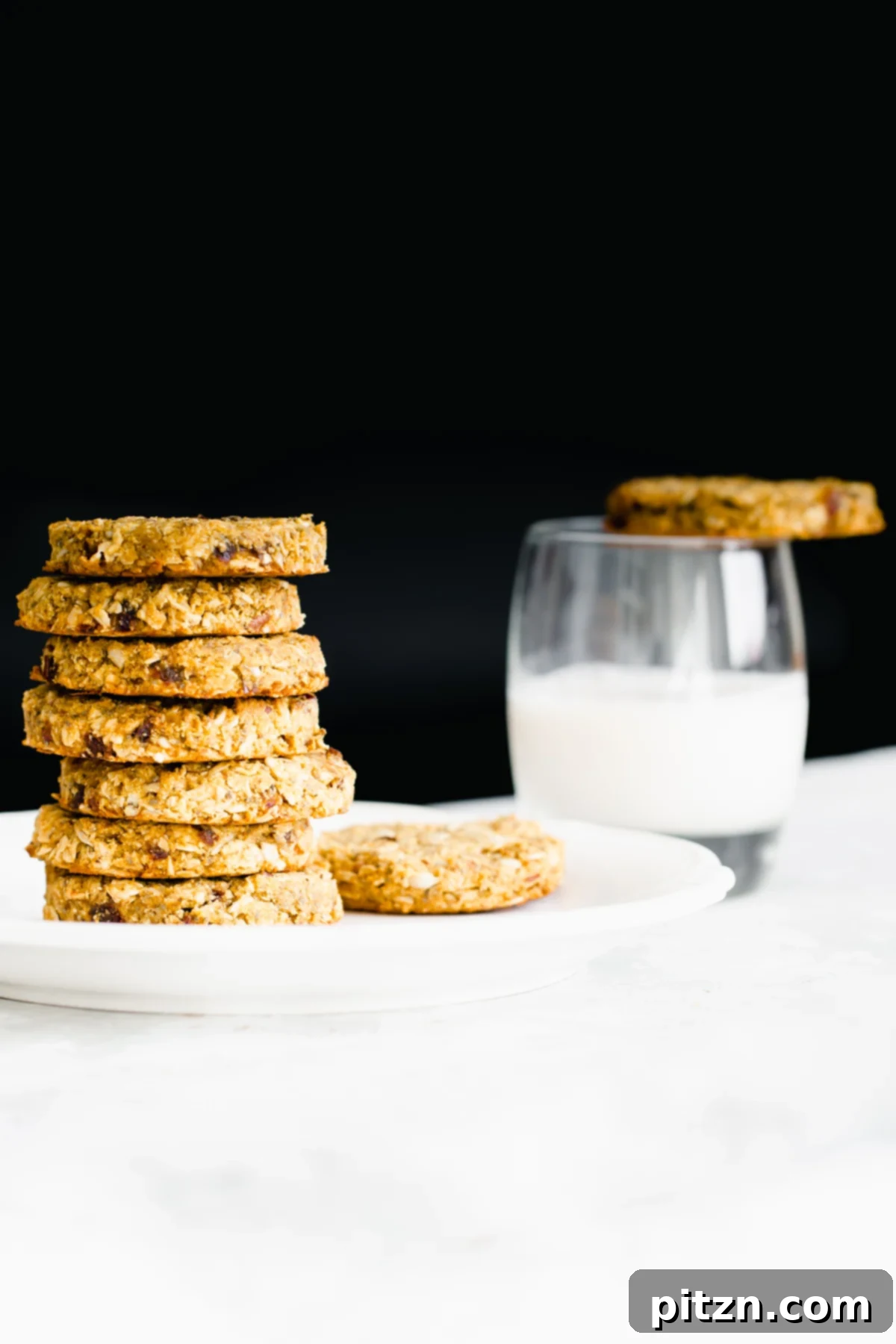 Ready to serve pumpkin breakfast cookies Stacked pumpkin breakfast cookies on a white plate with a glass of plant-based milk in the background, offering a cozy breakfast scene.