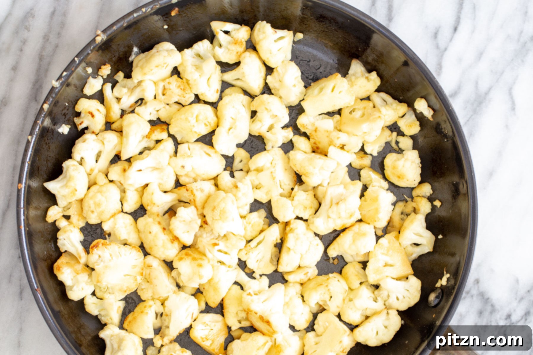 Rich Double Onion Cauliflower 6 Cauliflower florets sizzling and turning golden brown in a sauté pan, preparing for the Gobi Do Pyaza.