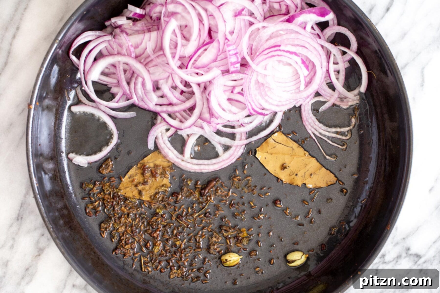 Rich Double Onion Cauliflower 8 Thinly sliced onions and a mix of whole spices (cumin, bay leaves, cardamom, clove) are sautéing in a black skillet, beginning to soften and caramelize for the curry base.