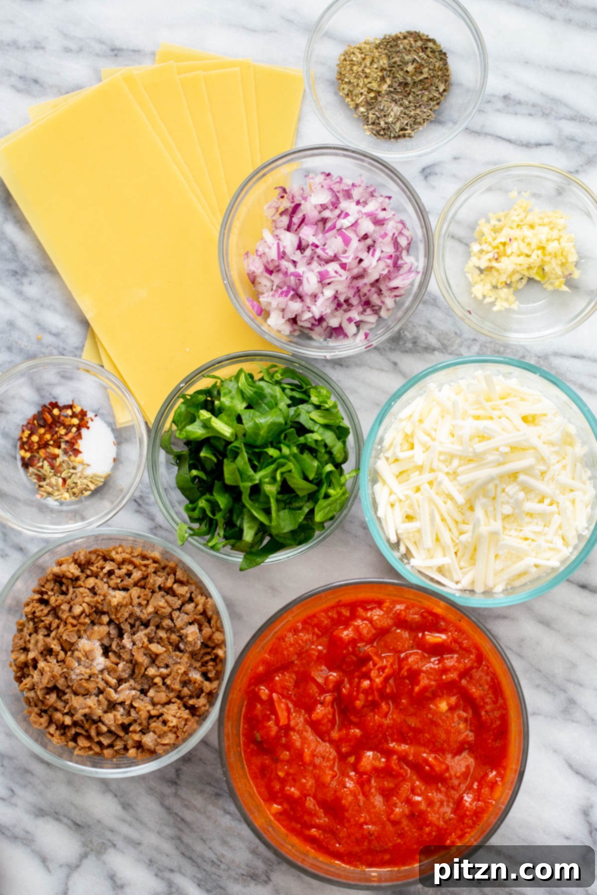 Hearty Vegan Skillet Lasagna 6 A flat lay photograph showcasing all the ingredients required for making a vegan skillet lasagna, including pasta, marinara, vegan crumbles, herbs, and cheese.
