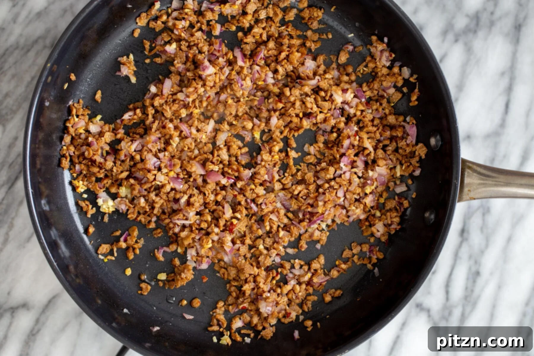 Hearty Vegan Skillet Lasagna 9 The veggie crumbles, sautéed onions, and garlic cooking together in a black skillet, becoming golden and fragrant as they develop their rich 'meat' flavor.