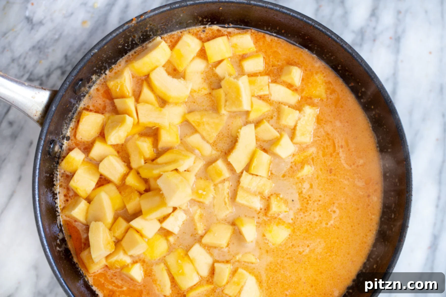 Freshly cubed pumpkin pieces being added to the simmering coconut milk curry broth in a saucepan.