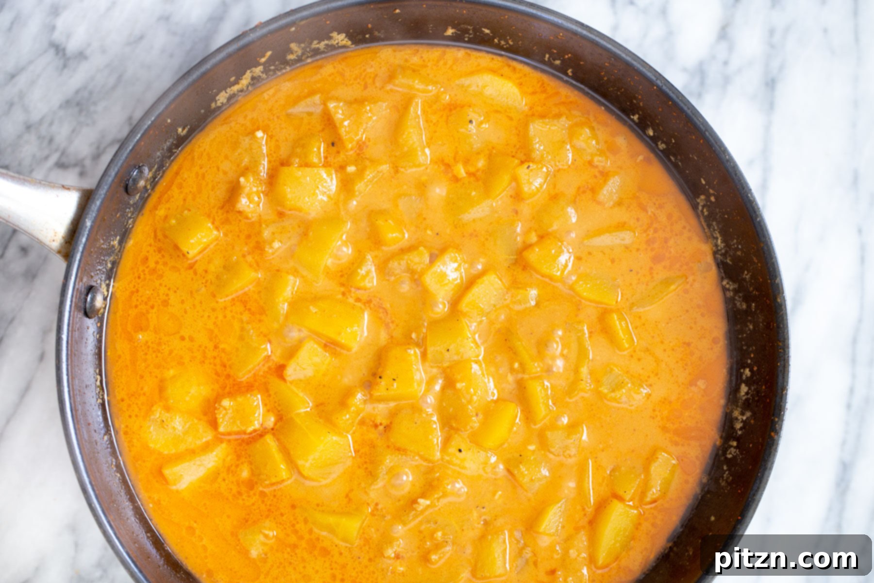 Cubed pumpkin simmering gently in a vibrant orange Thai coconut curry broth, softening as it cooks.