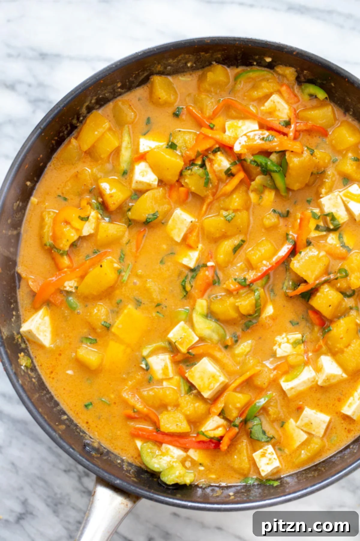 A large saucepan filled with creamy Thai Pumpkin Curry, featuring tender pumpkin pieces and cubed tofu, ready to be served.