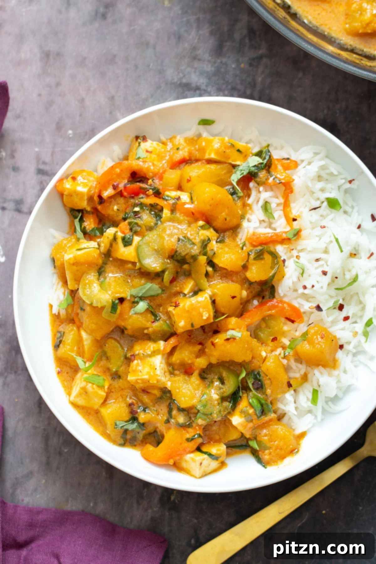 A beautifully presented bowl of Vegan Thai Pumpkin Curry, served with a side of white rice, garnished with fresh basil and a lime wedge.
