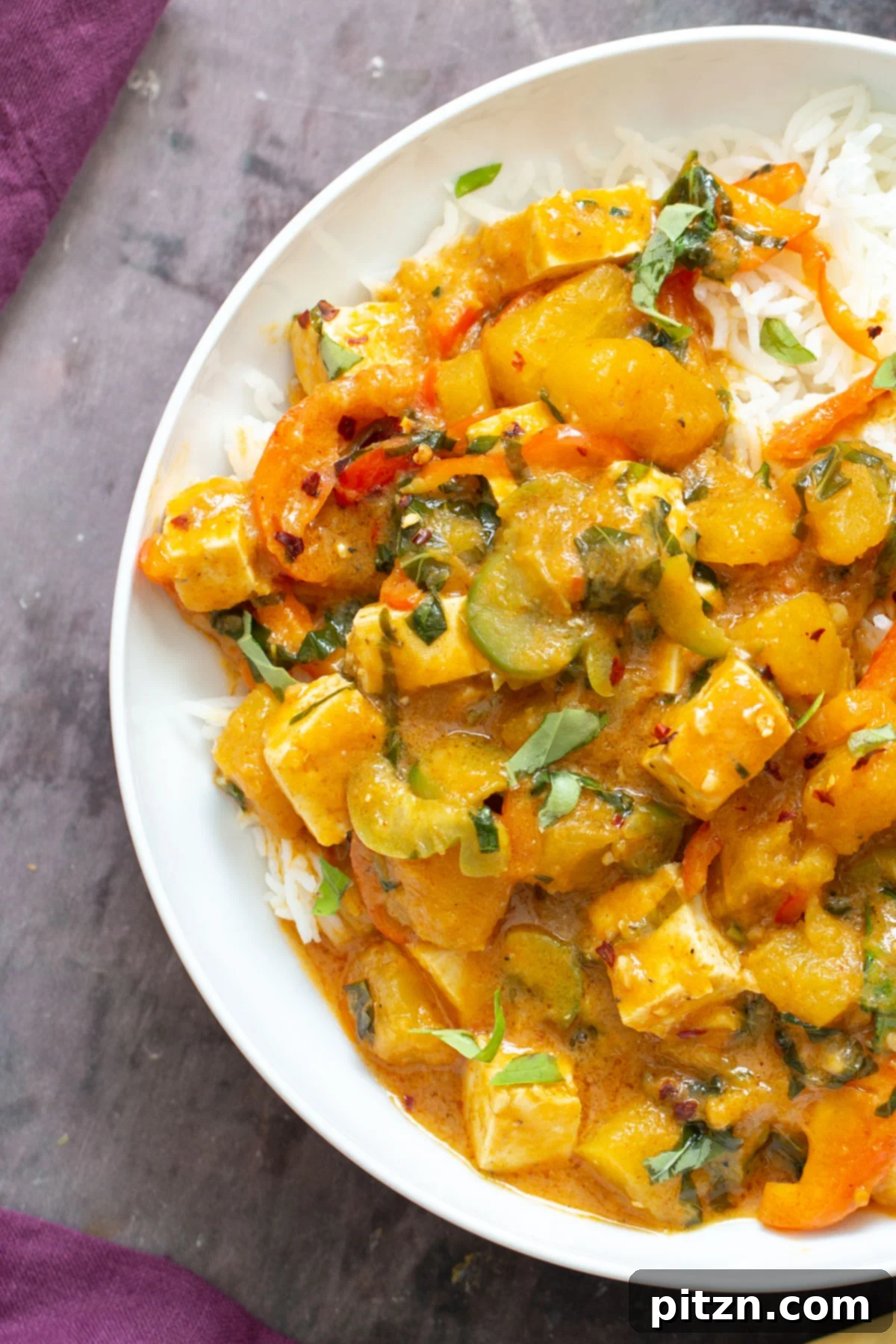 A close-up of a white plate holding a generous serving of Thai Pumpkin Coconut Curry, garnished with fresh basil leaves.