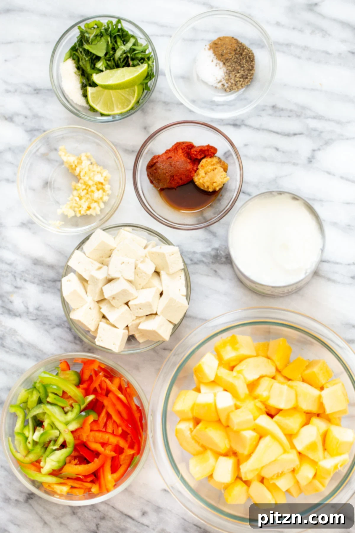 A vibrant collection of fresh ingredients laid out, including cubed pumpkin, bell peppers, fresh Thai basil, a can of coconut milk, and various spices, all ready for cooking.