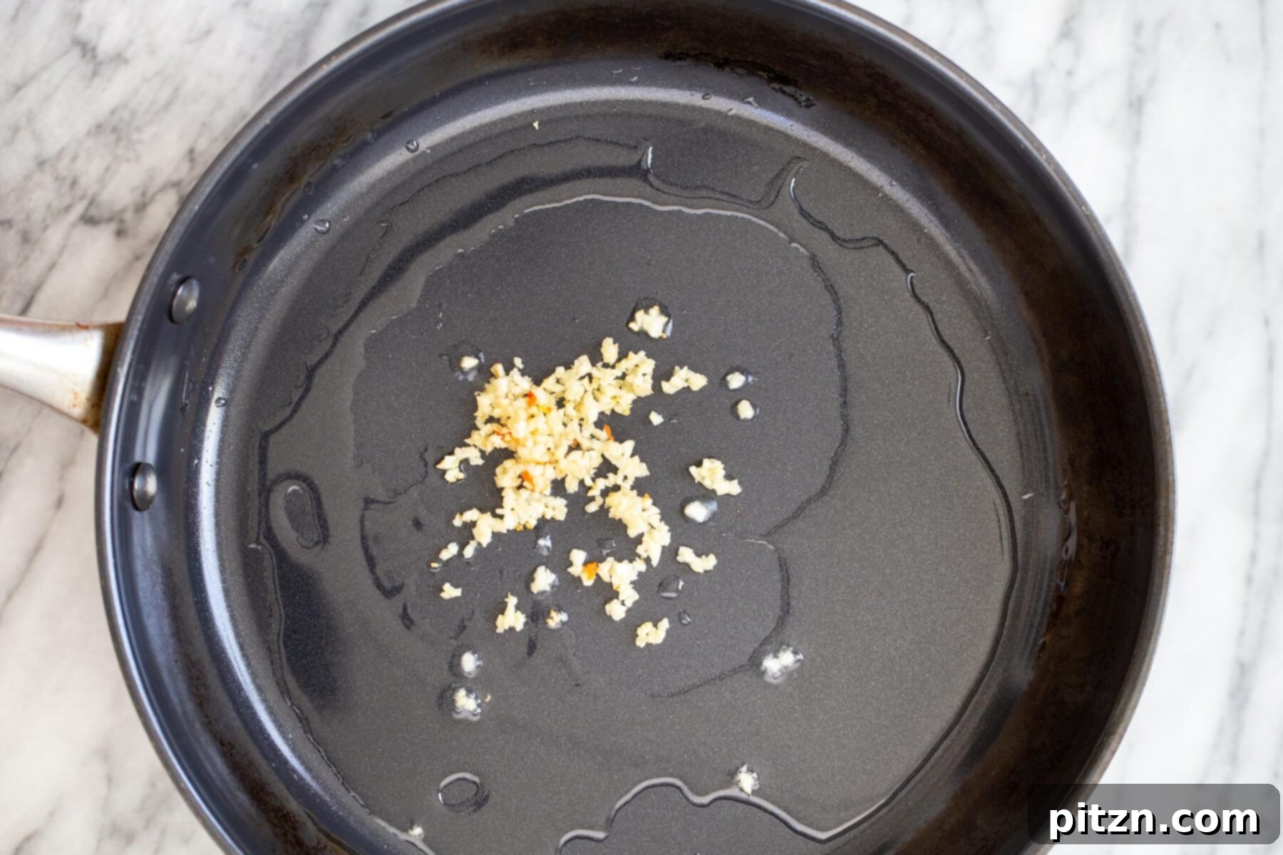 Minced garlic cloves sizzling gently in a small amount of oil in a saucepan, turning golden brown.