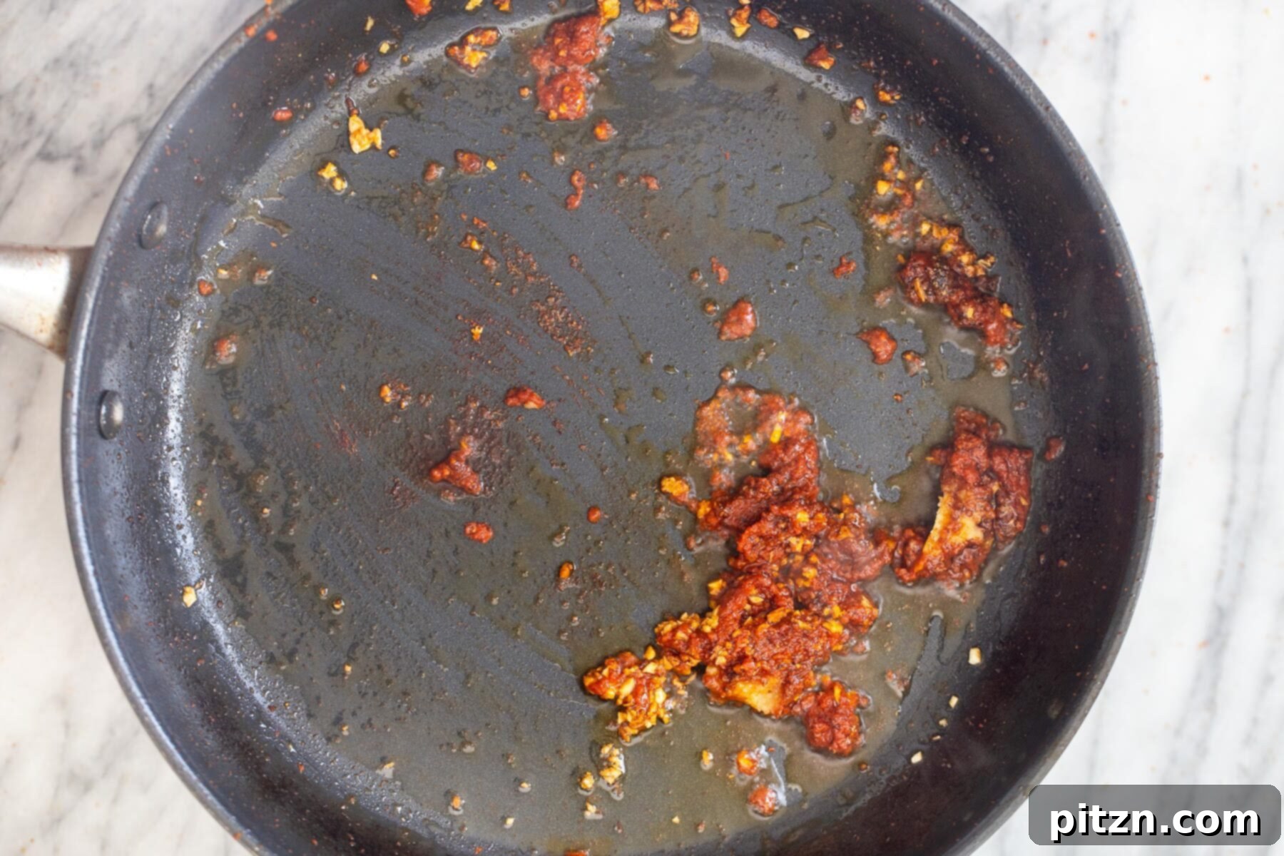 Minced garlic and vibrant red curry paste mixed together in a saucepan, releasing rich aromas as they sauté.