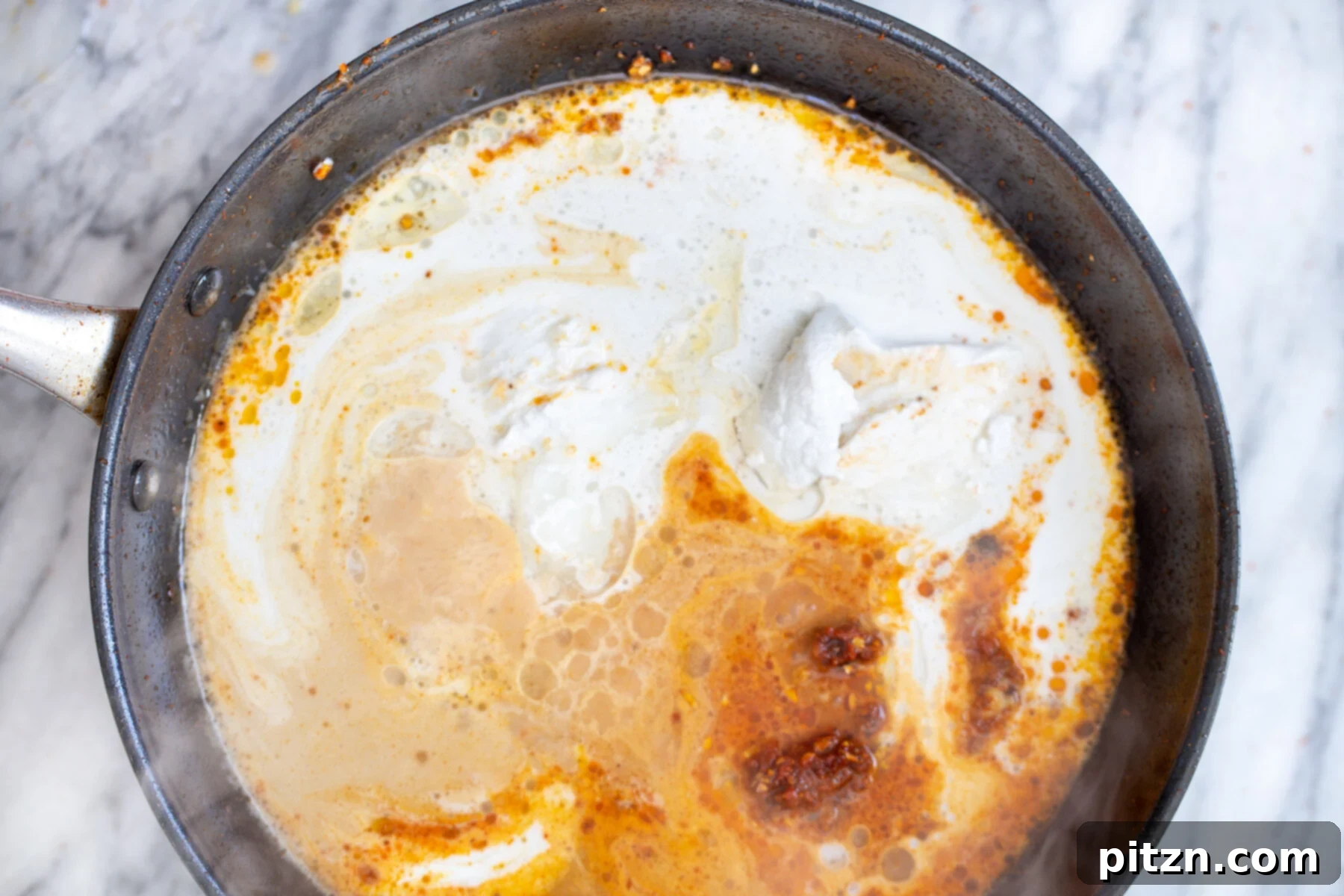 A can of creamy coconut milk being poured into a saucepan with the red curry paste and aromatics, ready to form the curry broth.