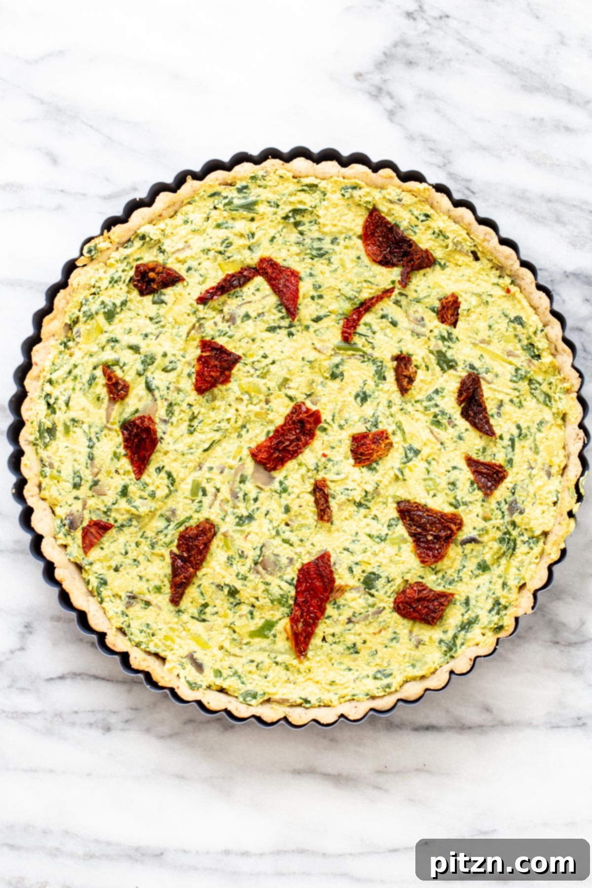 Garden Fresh Vegan Quiche with Mushrooms, Spinach and Leeks 9 Unbaked vegan quiche with a rich filling of mushrooms, spinach, and leeks in a tart pan, topped with cherry tomatoes, ready for baking.