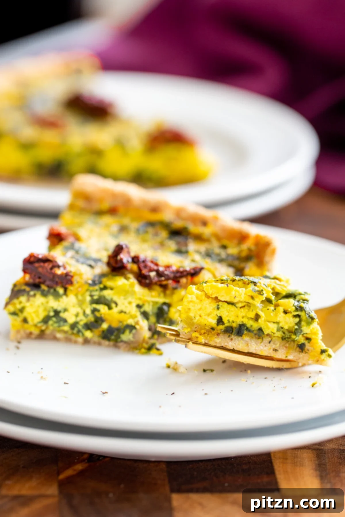 Garden Fresh Vegan Quiche with Mushrooms, Spinach and Leeks 10 A fork gently lifts a piece from a slice of freshly baked vegan quiche, showing the fluffy tofu filling and vibrant vegetables within the golden crust.