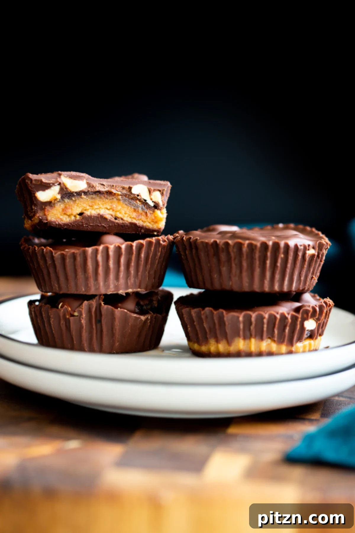 Two stacks of homemade vegan snickers peanut butter cups on a white plate, showcasing their layers of chocolate, nougat, dates, and peanuts.