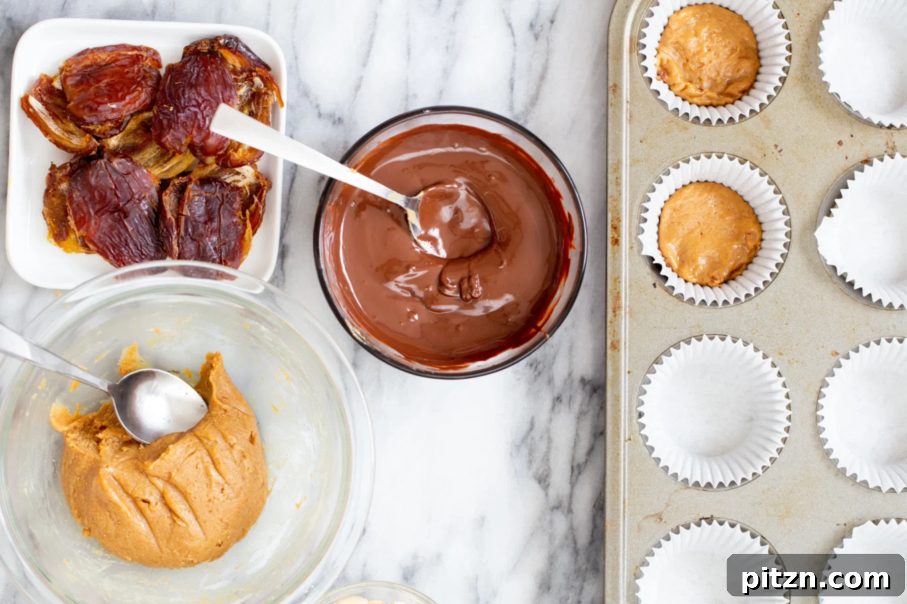 Mini muffin liners being filled with layers of melted chocolate and peanut butter nougat, ready for the next ingredient.