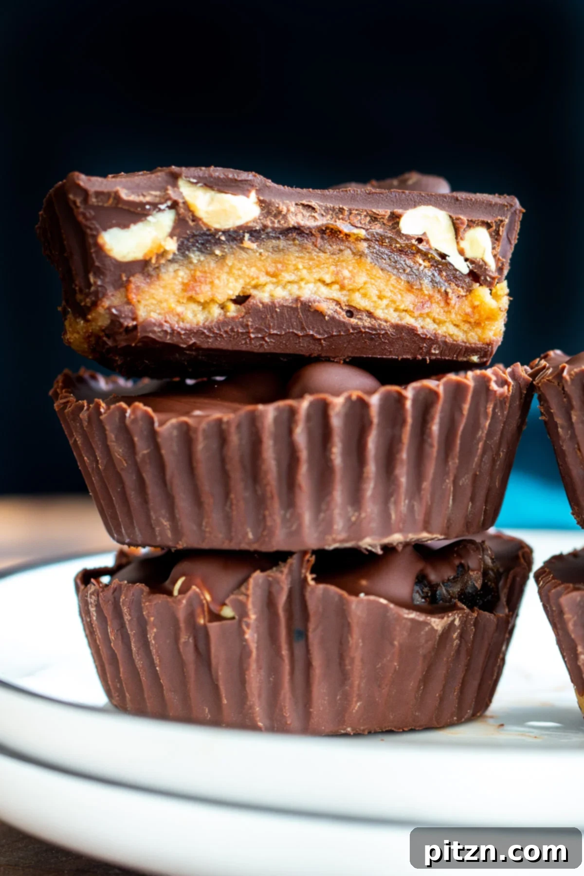A stack of vegan snickers cups on a white plate, with the date caramel layer visible in the cross-section.
