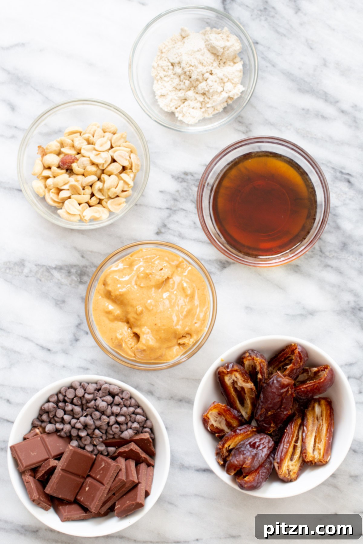 Ingredients for vegan peanut butter cups laid out on a marble surface, including chocolate chips, peanut butter, dates, and nuts.