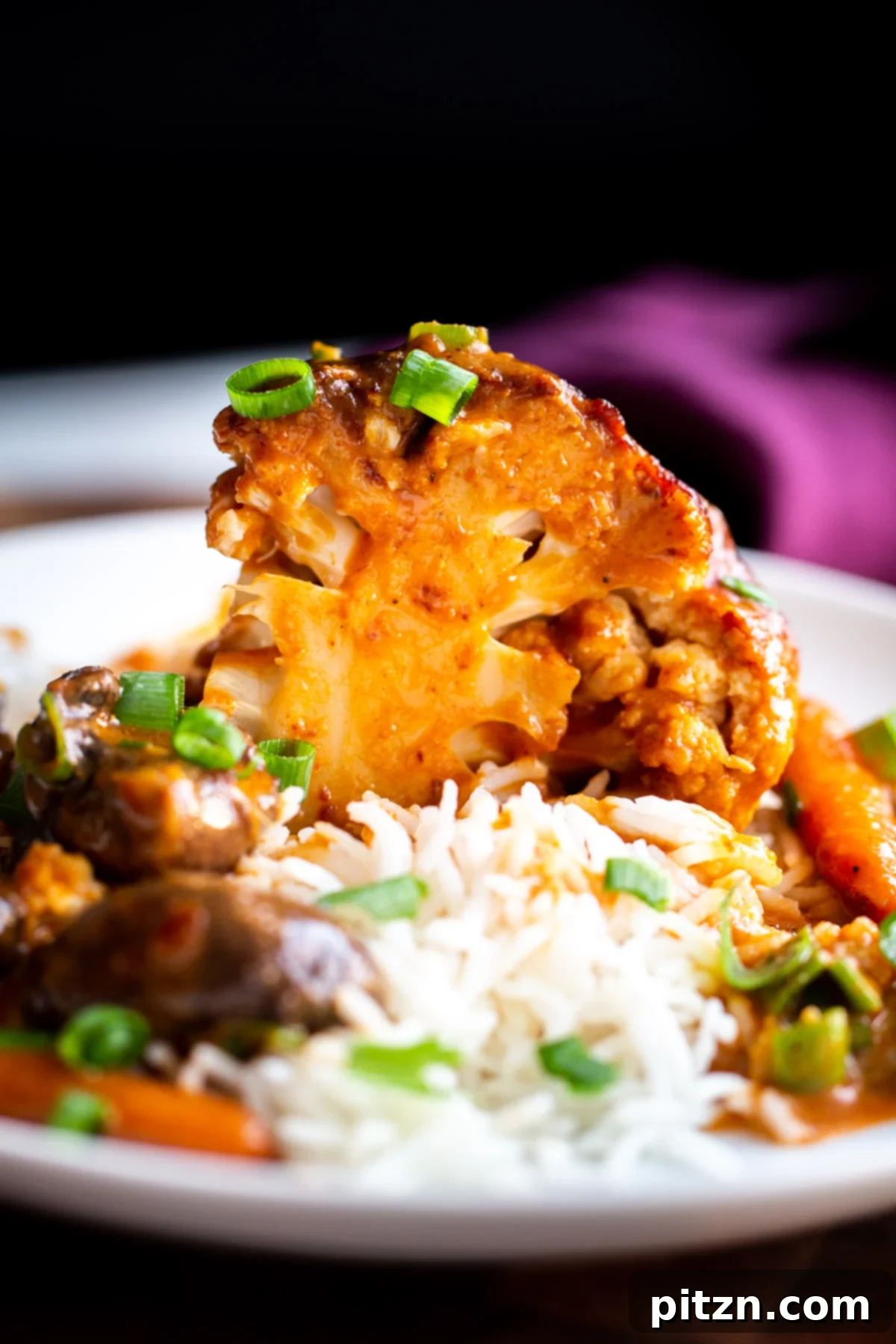 Miso Roasted Cauliflower A wedge of a whole glazed peanut butter miso roasted cauliflower served with rice and garnished with green onions.