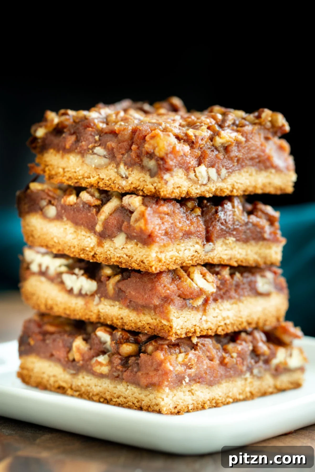 Delicious Vegan Pecan Pie Bars A beautiful stack of vegan gluten-free pecan pie bars on a crisp white plate, showcasing their delightful layers and golden-brown crust.