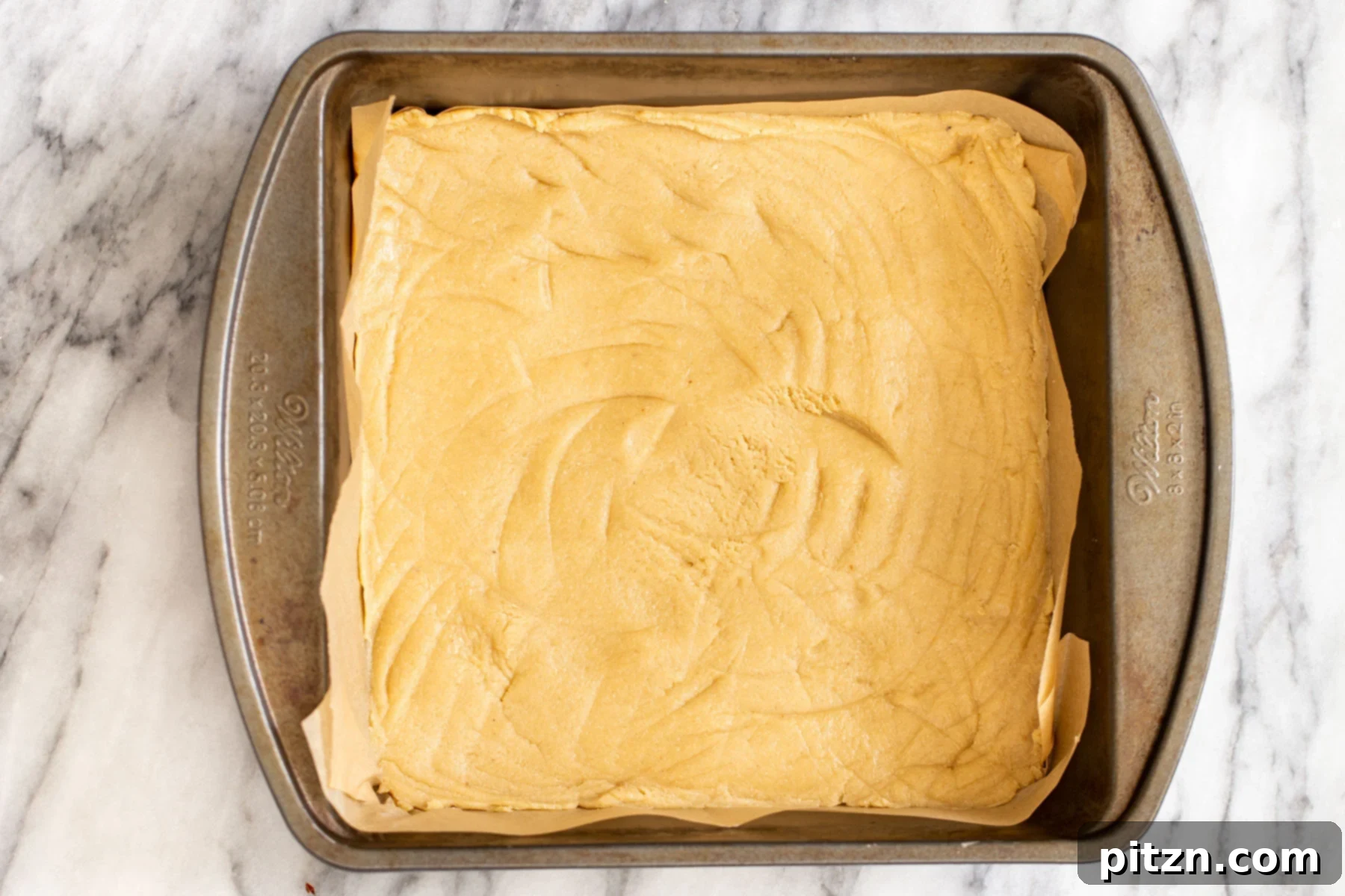 Unbaked Cookie Crust in Pan The unbaked cookie crust pressed firmly into a baking pan lined with parchment paper, awaiting its first bake.