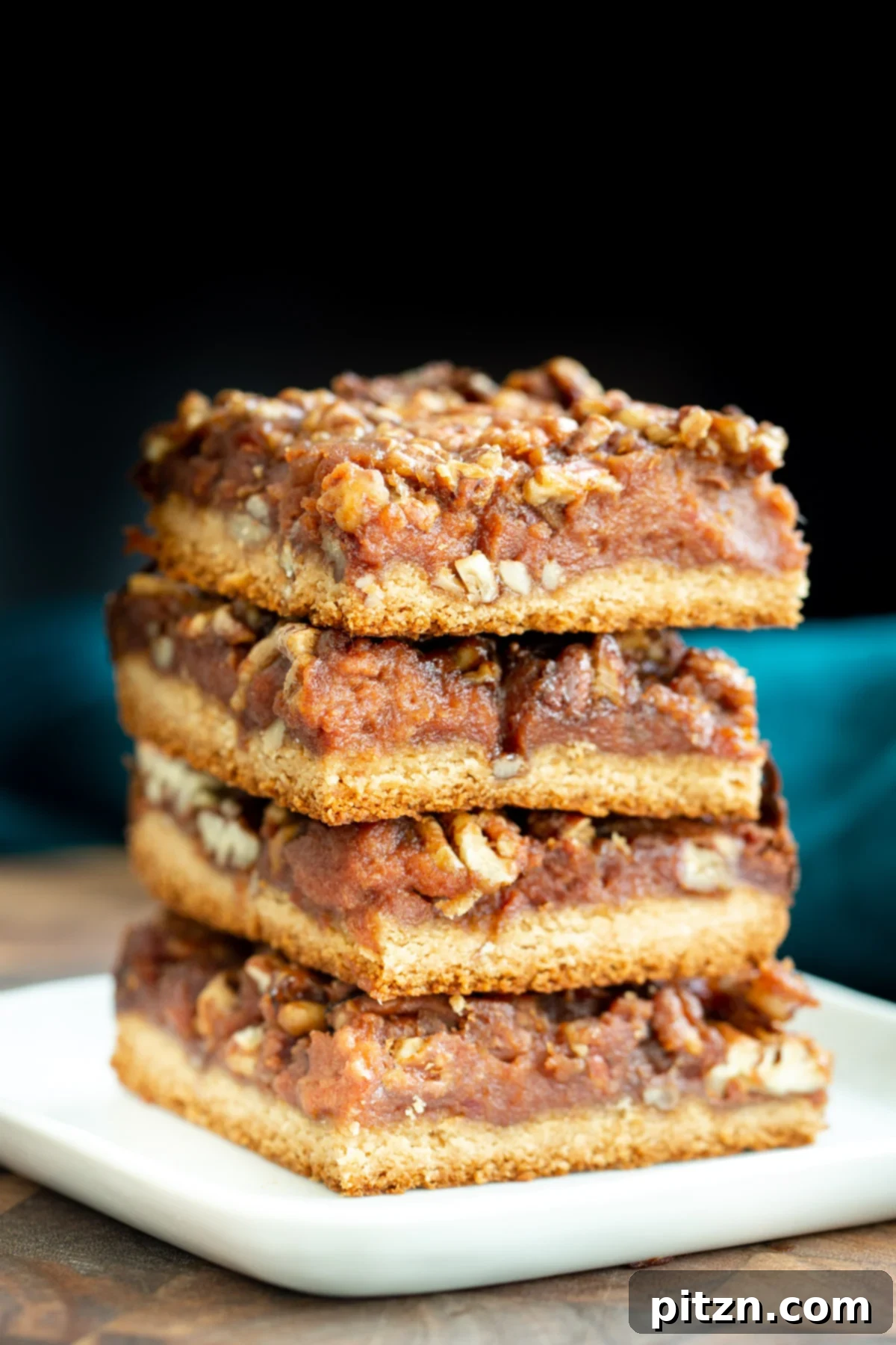 Stacked Vegan Pecan Pie Bars A high stack of vegan gluten-free pecan pie bars, glistening with caramel and pecans, ready for a close-up.