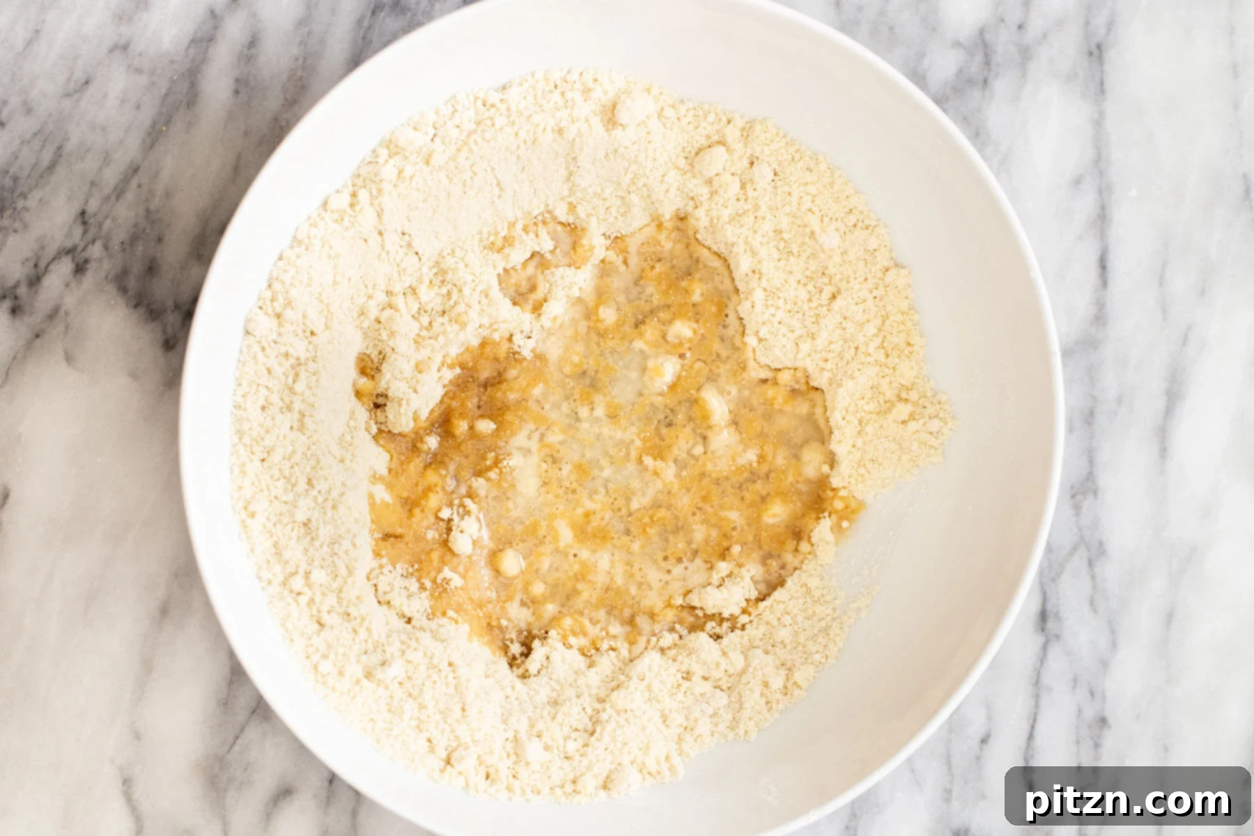 Adding Coconut Oil to Crust Mix Melted coconut oil being poured into the dry flour mixture to create the base for vegan pecan pie bars.