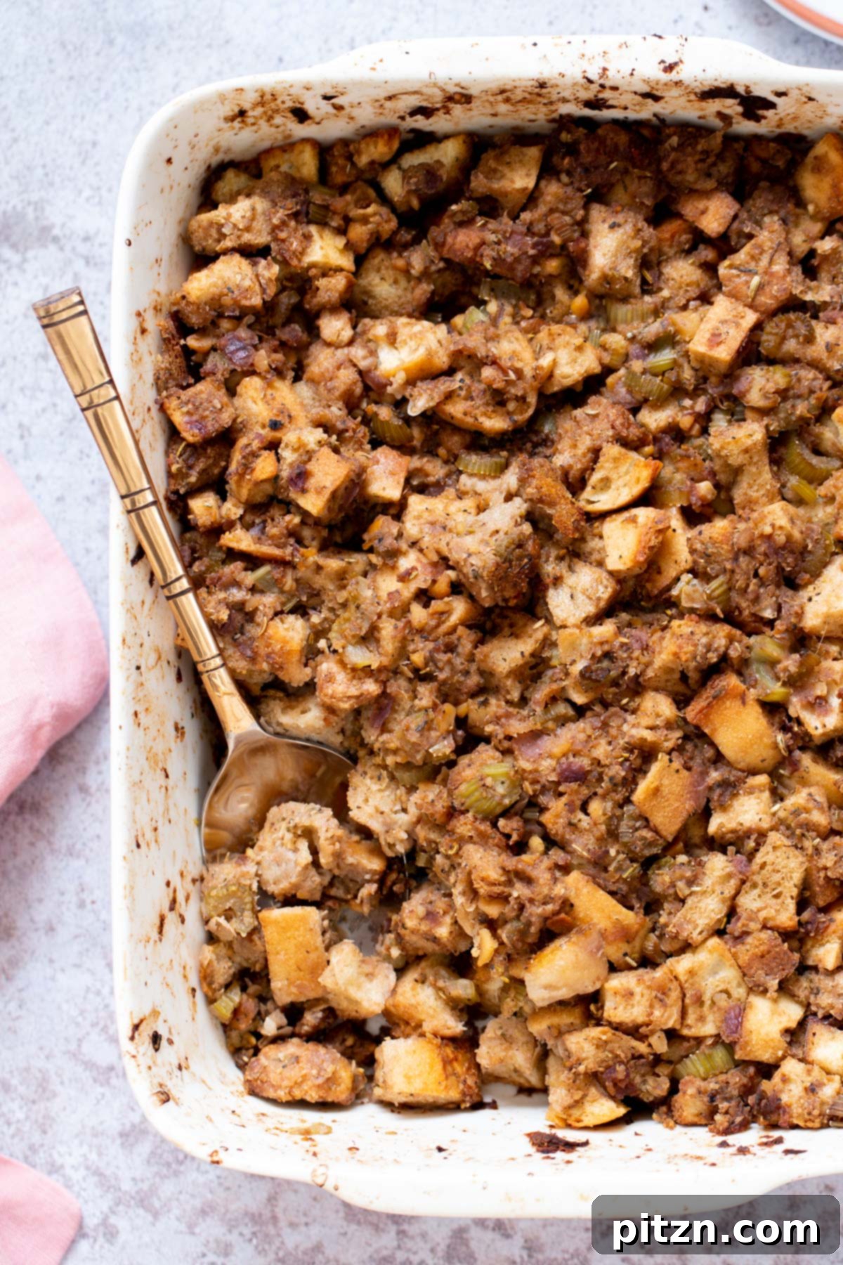 A casserole dish filled with golden-brown vegan stuffing, featuring visible chickpea sausage crumbles and herbs.