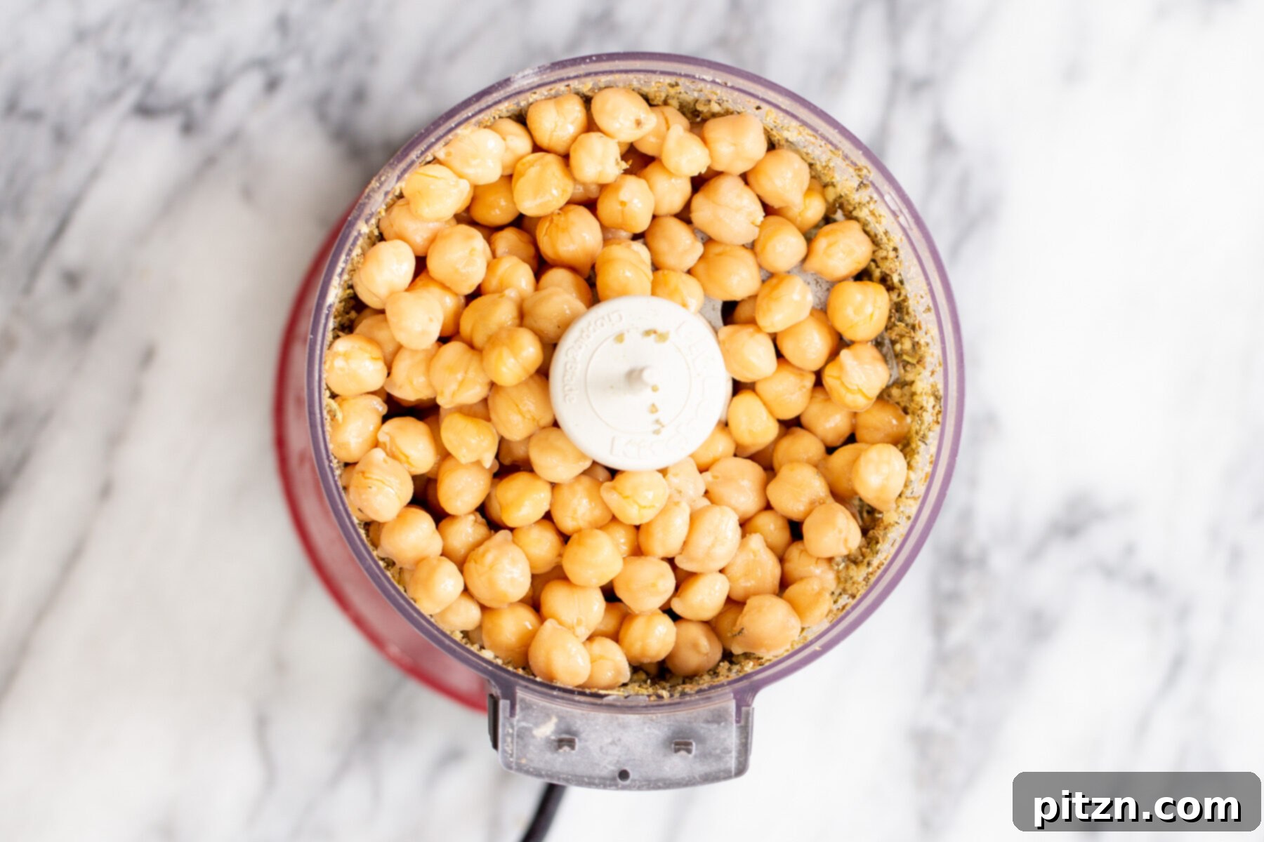 Cooked chickpeas being added to the food processor with the spiced walnut mixture, for the vegan sausage crumbles.
